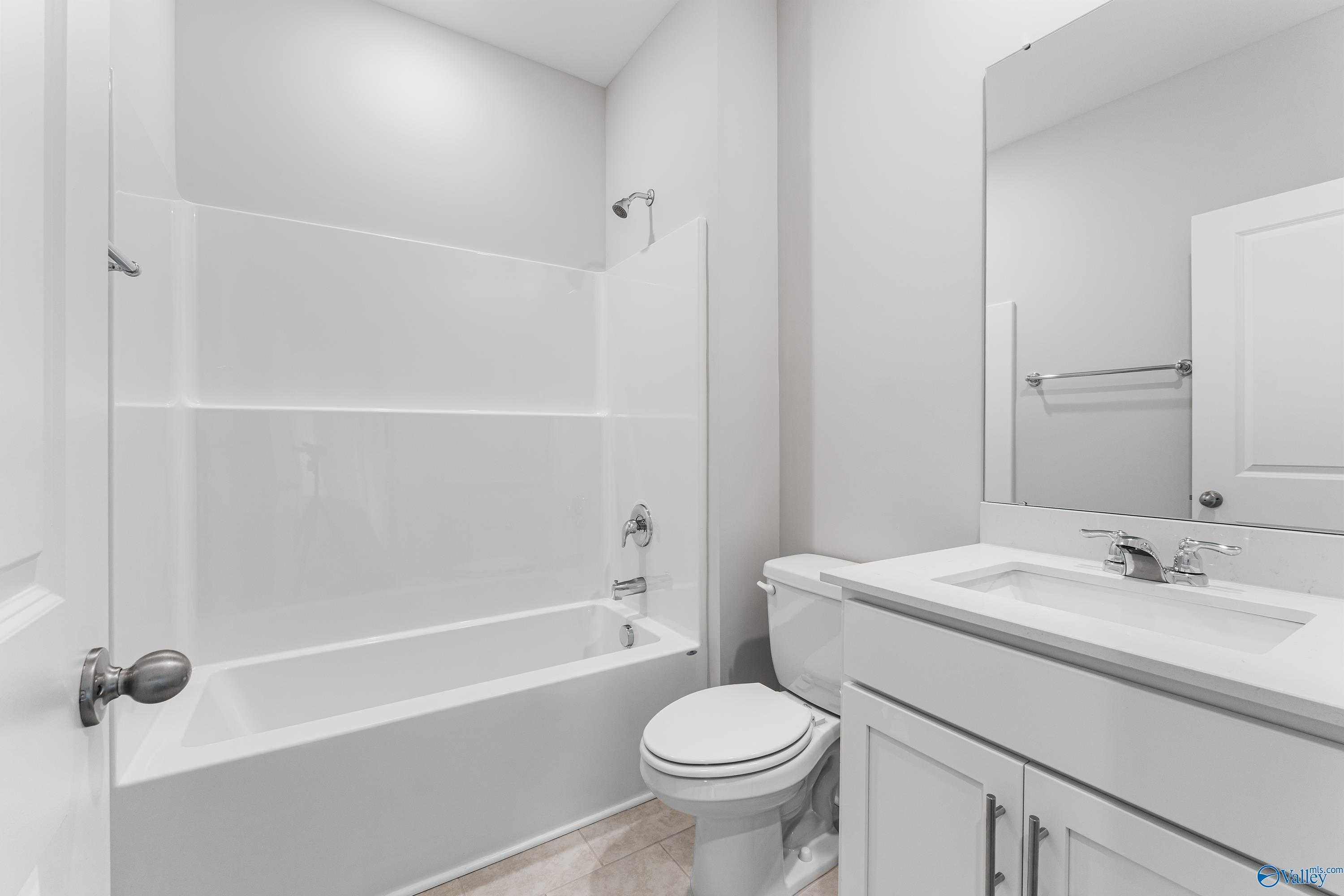 Modern white guest bathroom with soaking tub, shower combo, vanity sink, and toilet in Davidson Homes Madison A, Toney, AL