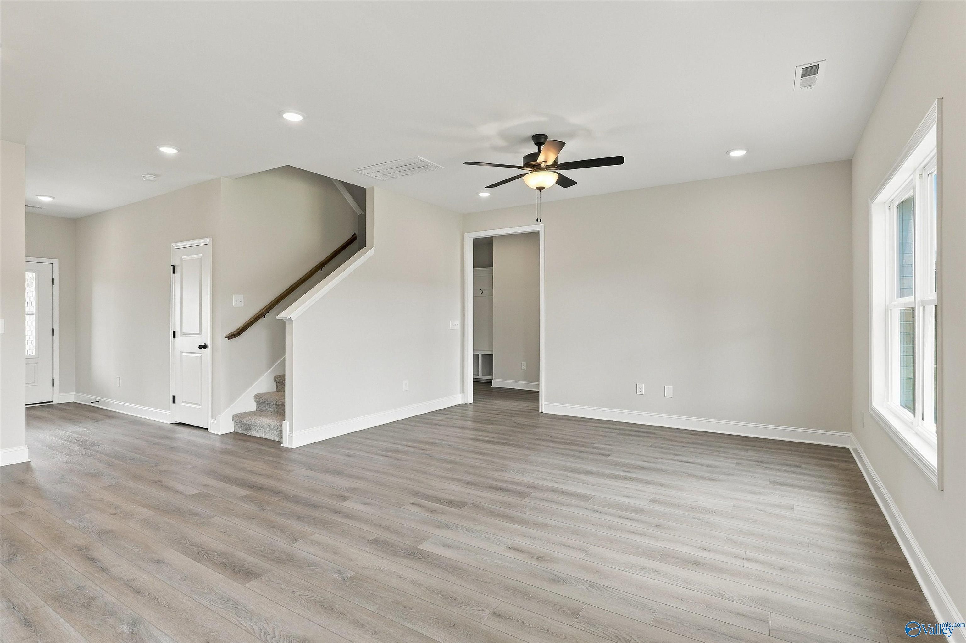 Open-concept living area with luxury vinyl plank flooring, staircase, and ceiling fan in Davidson Homes The Shelby A, Athens, AL