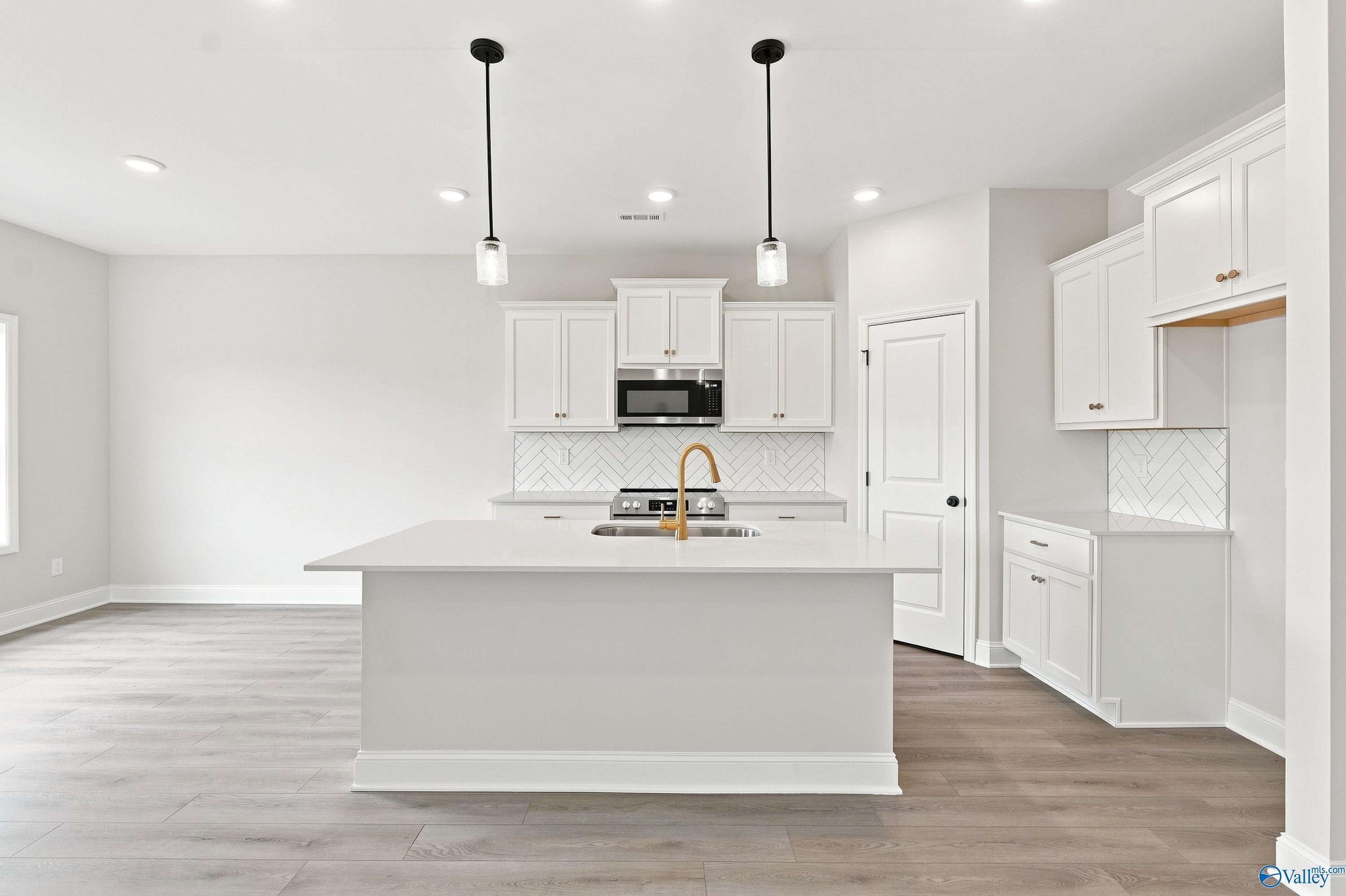 Modern kitchen with white cabinets, center island, and herringbone backsplash in The Asheville E, Forest Glen, Hazel Green.