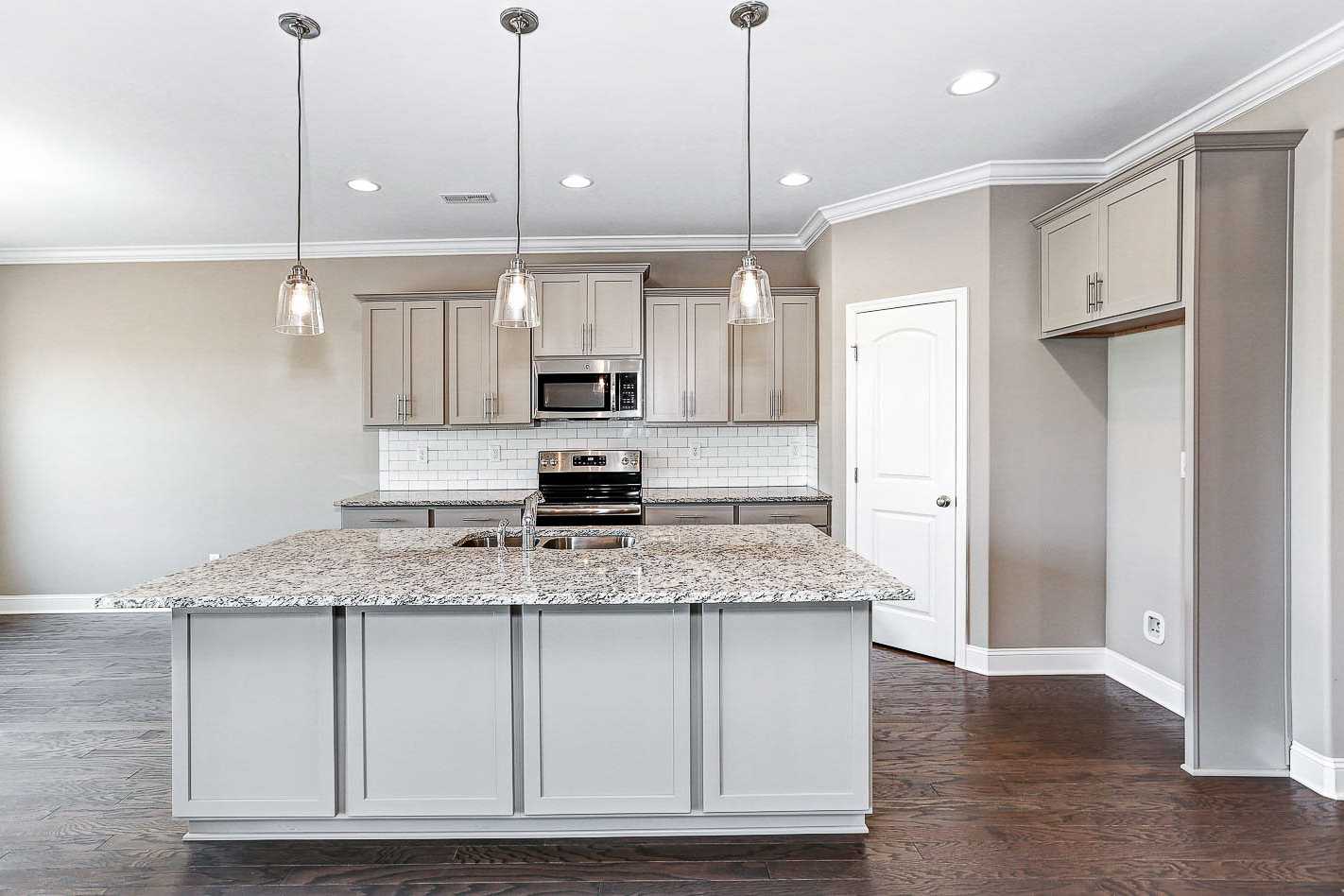 Spacious kitchen in The Montgomery by Davidson Homes featuring large granite island, white cabinets, subway tile backsplash, and stainless appliances