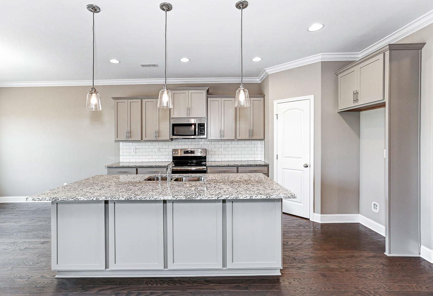 Spacious kitchen in The Montgomery by Davidson Homes featuring large granite island, white cabinets, subway tile backsplash, and stainless appliances