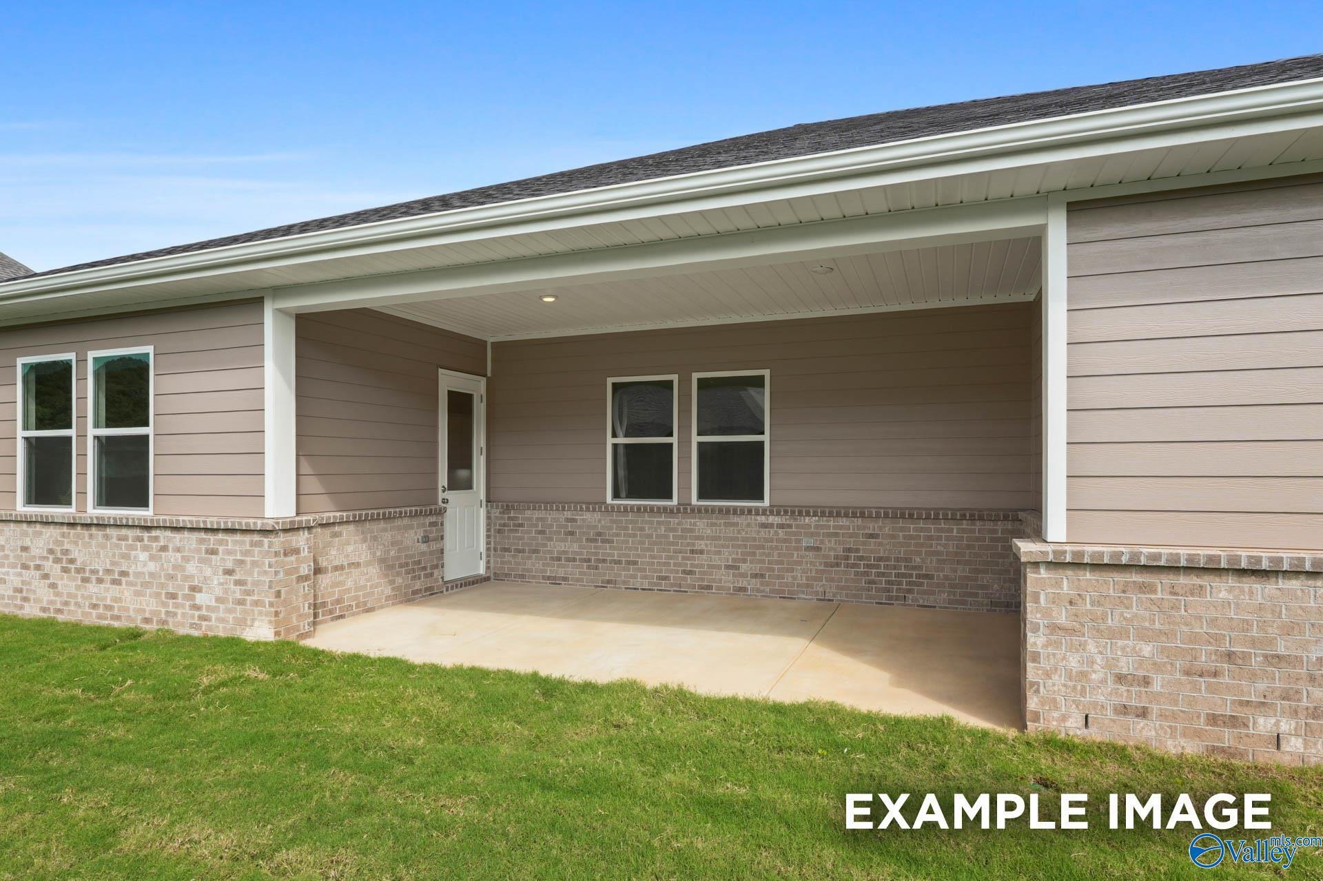 Covered porch with concrete patio and lush green lawn beside tan-sided 5-bedroom home, Evermore Homes The Haven E, Owens Cross Roads, Alabama