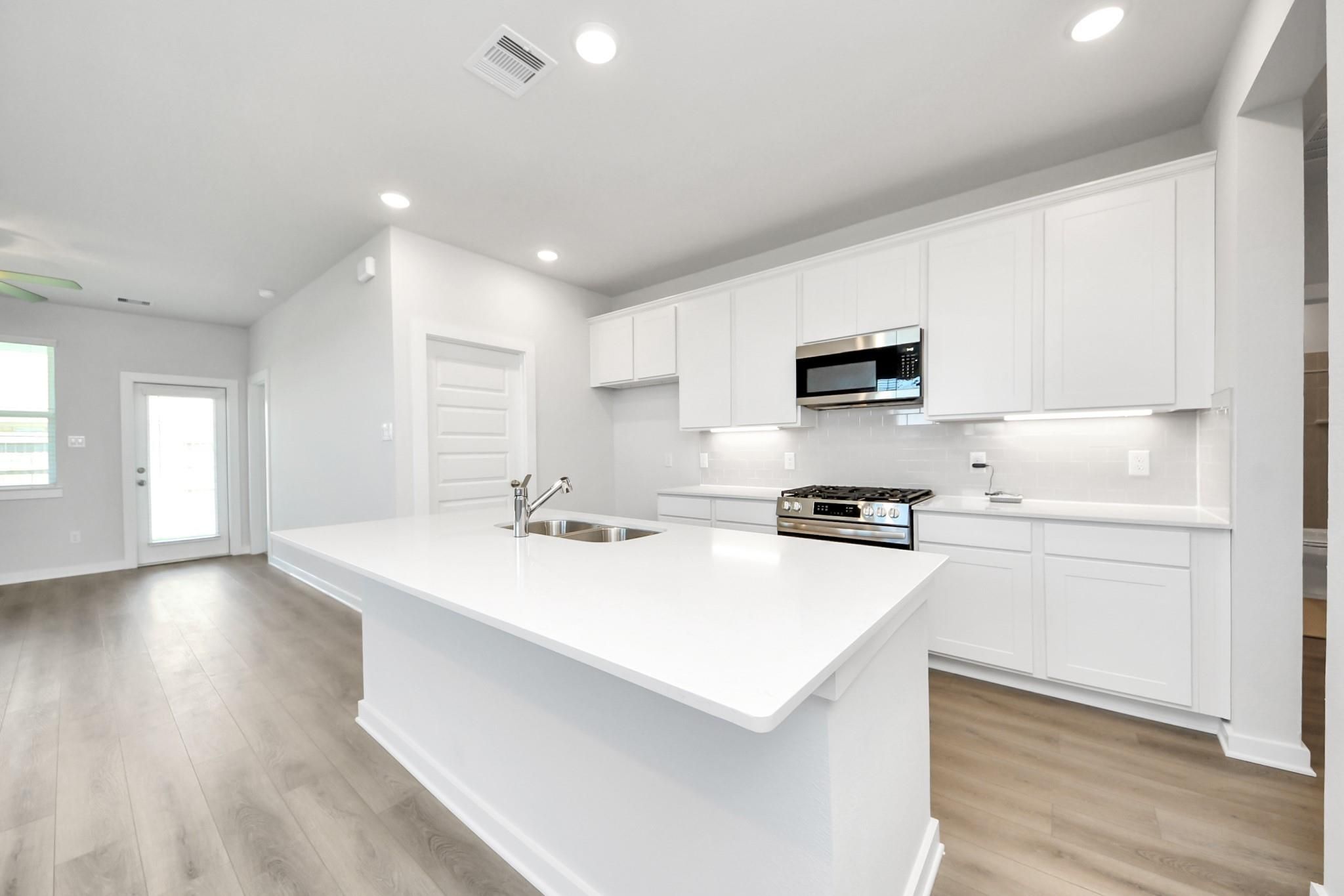 Modern kitchen with white cabinets, quartz island, and stainless appliances in The Costa A plan at Emberly, Beasley, Texas.