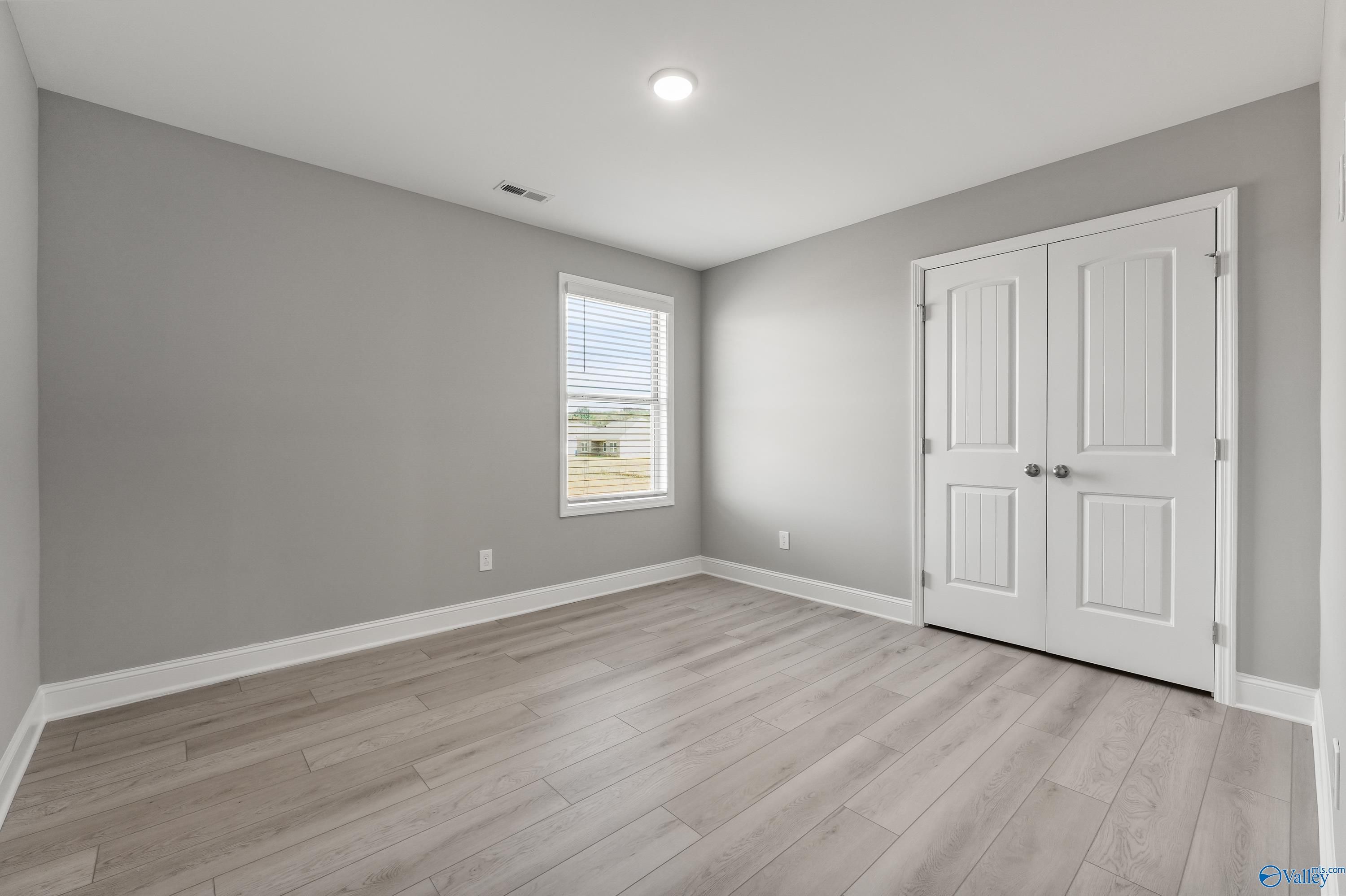 Spacious empty bedroom with gray walls, luxury vinyl plank floors, window blinds, and white double closet doors in Davidson Homes The Everett B, Athens AL