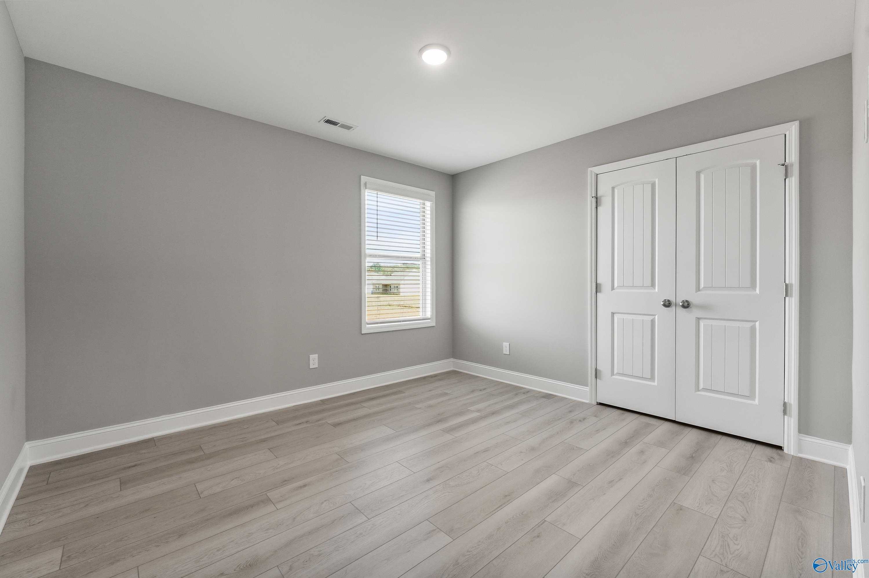 Bright secondary bedroom with gray walls, white double closet doors, window blinds, and light laminate floors in Davidson Homes The Everett B, Athens AL