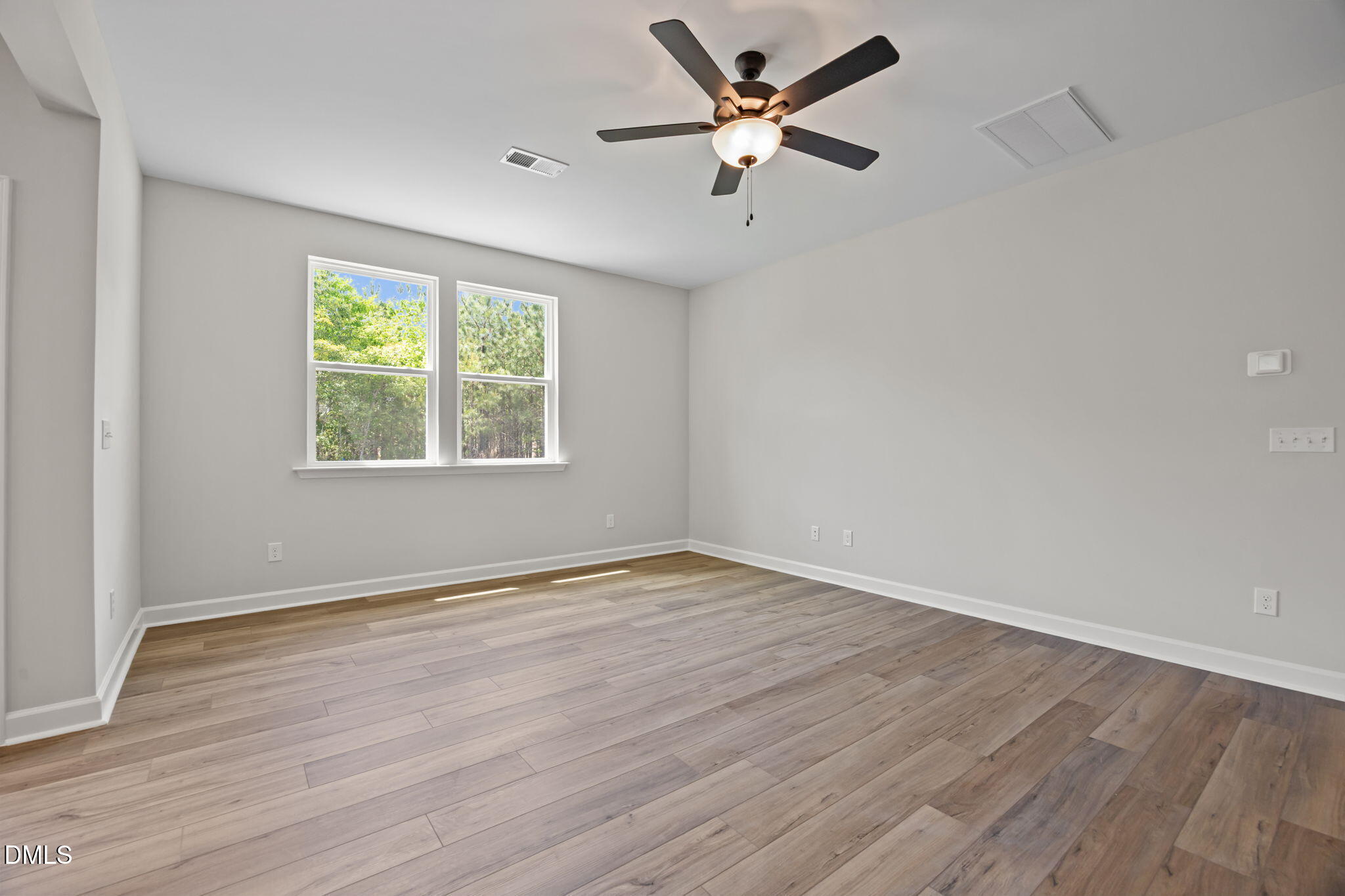 Bright bedroom with light gray walls, hardwood floors, ceiling fan, and large windows with tree views in The Willow D, Wendell, NC