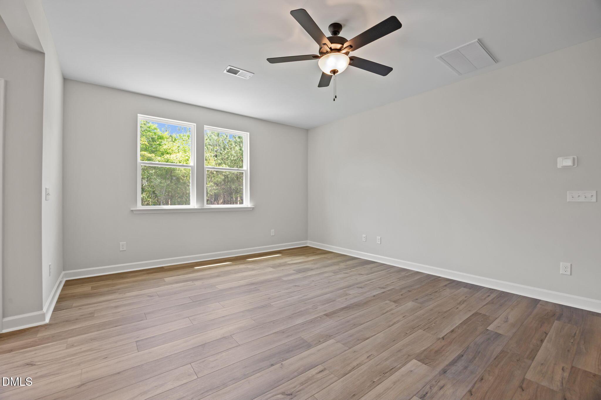 Bright bedroom with light gray walls, hardwood floors, ceiling fan, and large windows with tree views in The Willow D, Wendell, NC