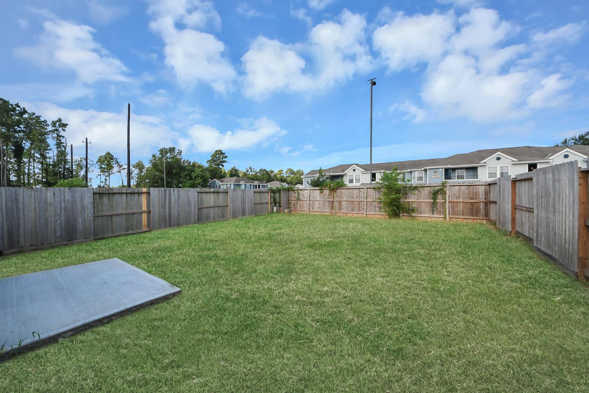 Spacious fenced backyard with lush green lawn and concrete patio at Davidson Homes The Frio F in Robins Landing, Houston, Texas