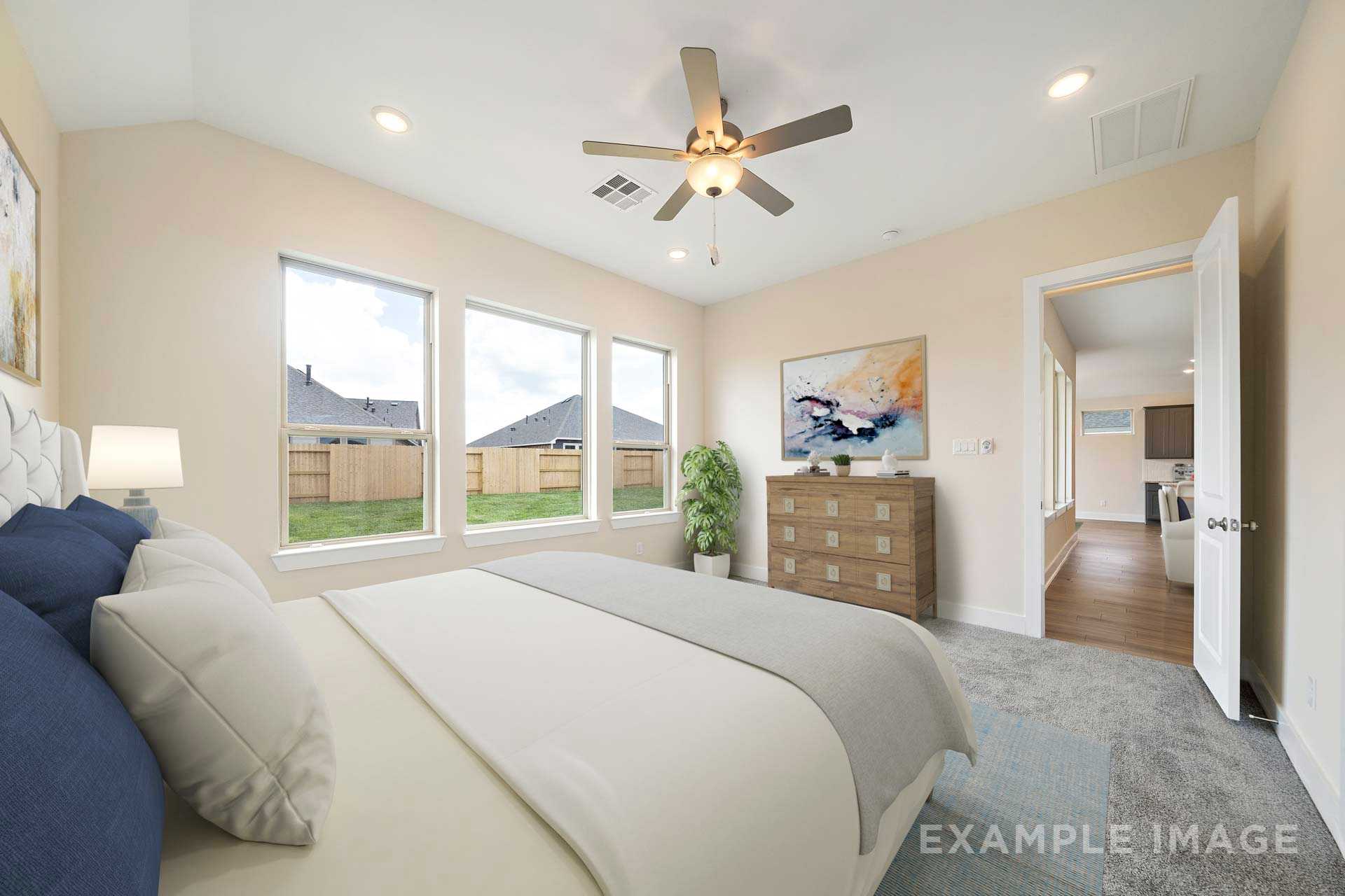 Spacious master bedroom in The Diana C by Davidson Homes with king bed, ceiling fan, large windows overlooking backyard, beige walls