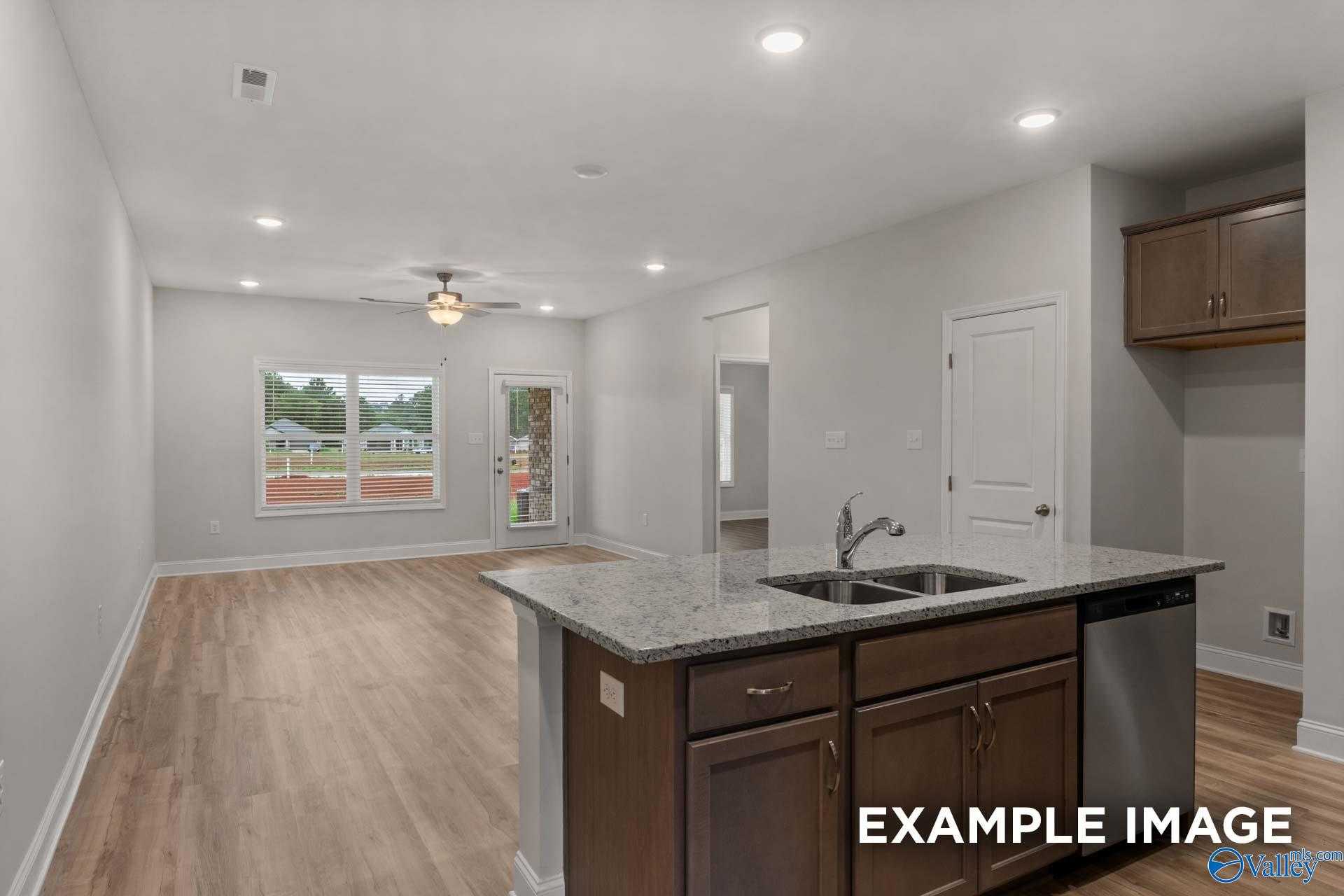 Open-concept living and kitchen with granite island, stainless sink, wooden cabinets, ceiling fan in Davidson Homes Cumberland B, Decatur, AL