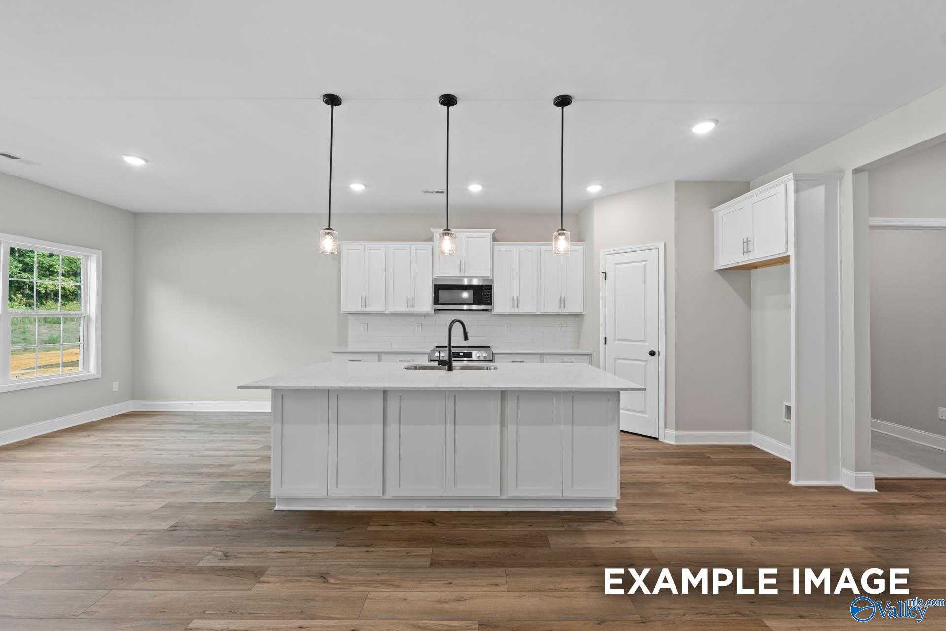 Modern white kitchen island with pendant lights and hardwood floors in Davidson Homes The Montgomery B, Toney, Alabama