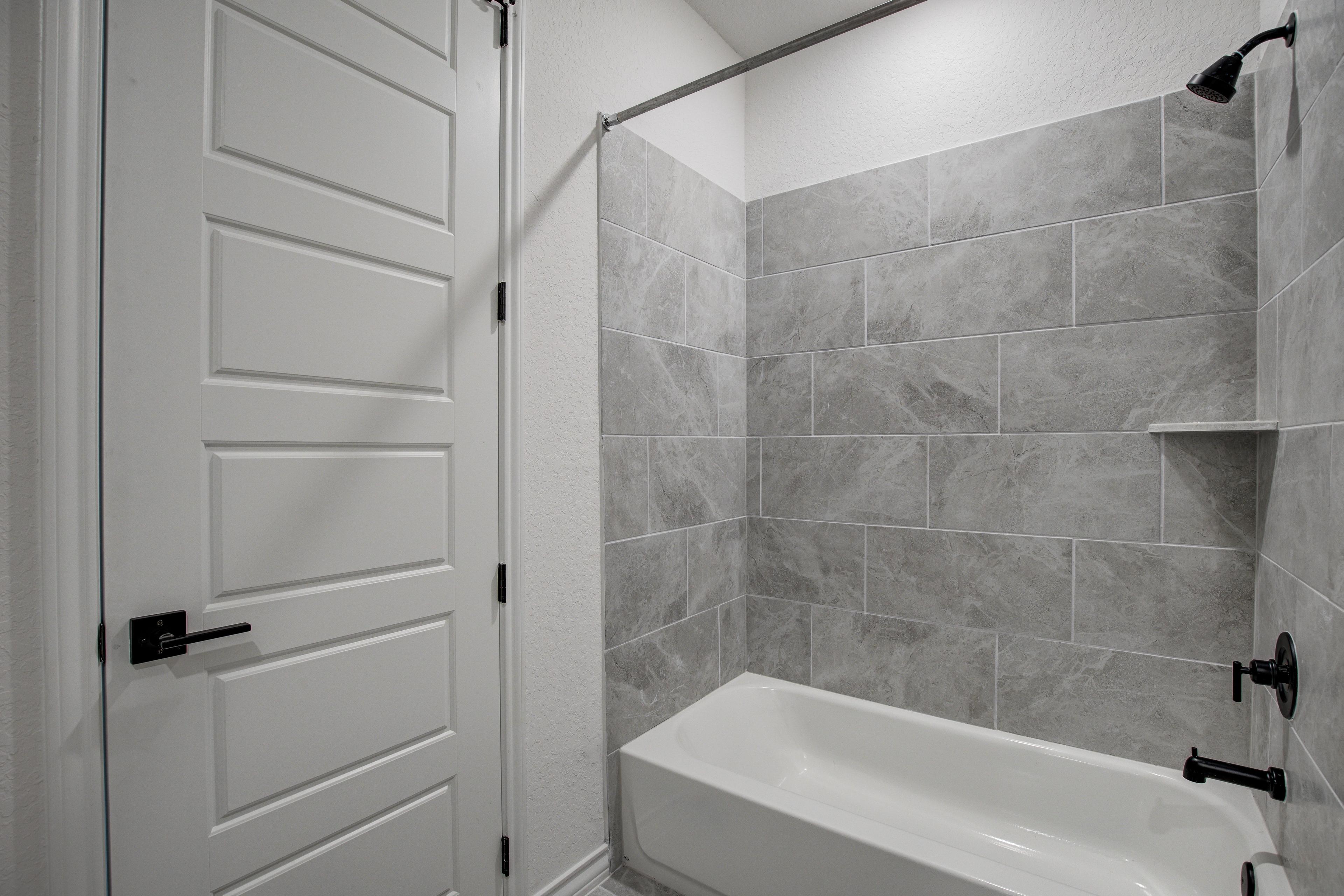 Master bathroom in The Lanier F showcasing gray subway tile shower, alcove soaking tub, and double entry doors
