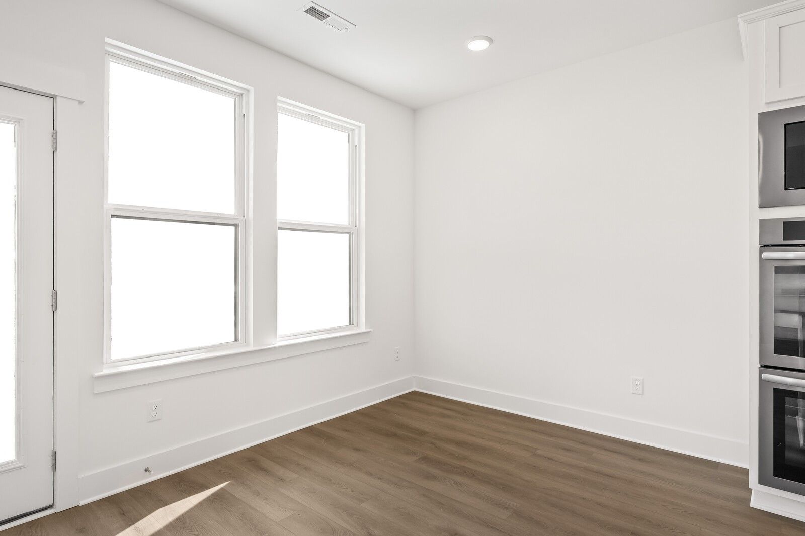 Bright kitchen featuring white cabinetry, double wall ovens, and large sunny windows in The Willow D, Mt. Juliet, TN
