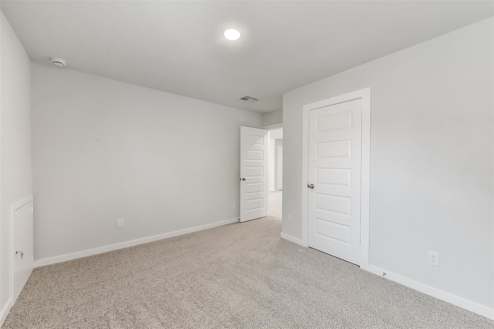 Empty bedroom with beige carpet, white walls, open door to bathroom in Davidson Homes The Brazos E, Magnolia, Texas