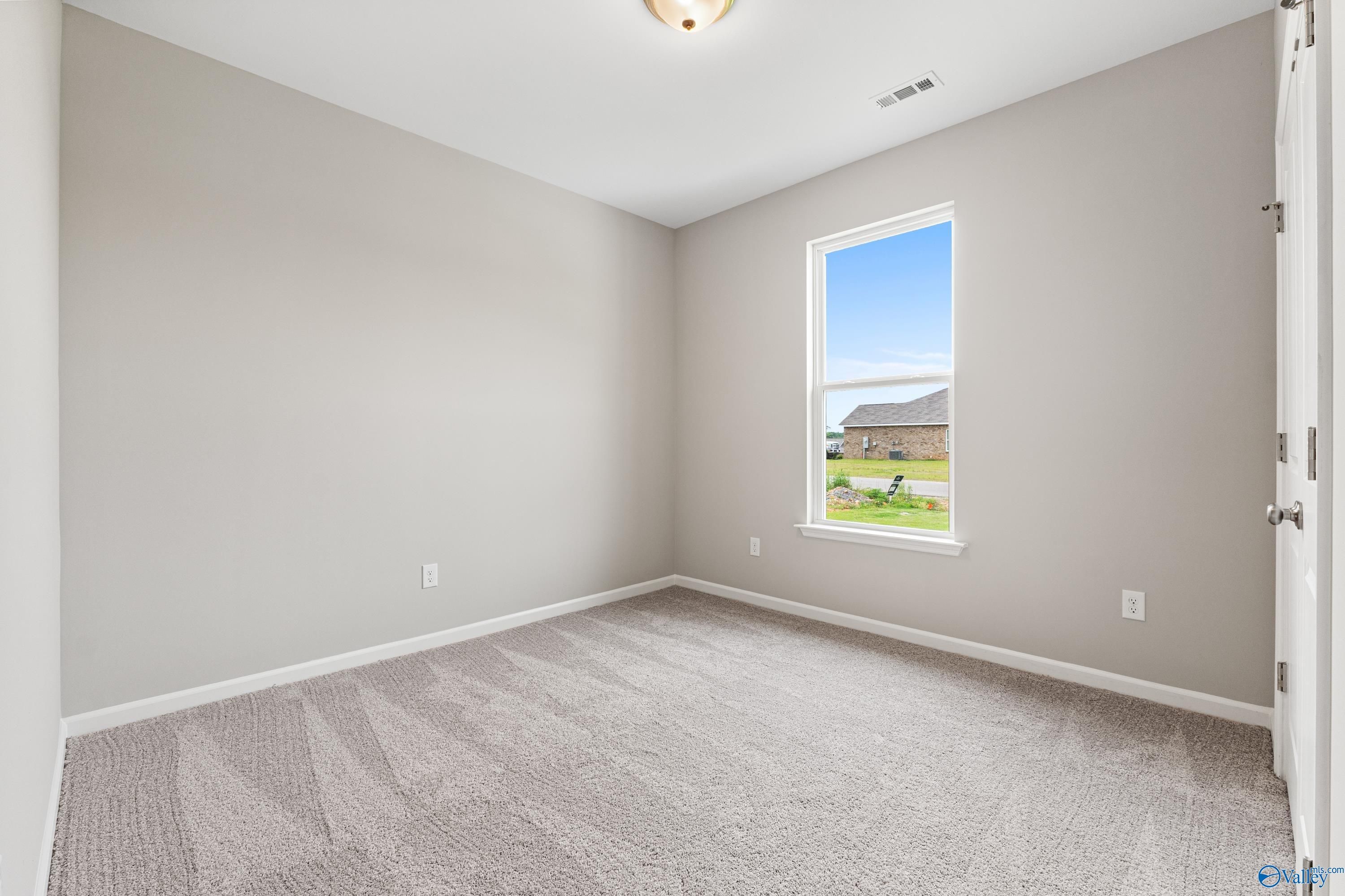 Cozy bedroom with light gray walls, plush carpet, and large window overlooking backyard in Davidson Homes The Aurora, Fayetteville, TN