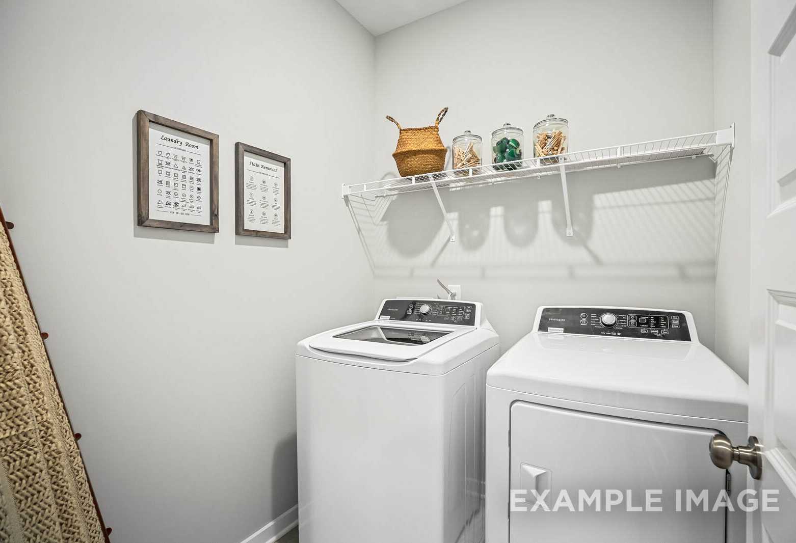 The Franklin C laundry room featuring white washer dryer, wire shelving with wicker baskets, glass jars, framed art, and woven ladder in Davidson Homes design