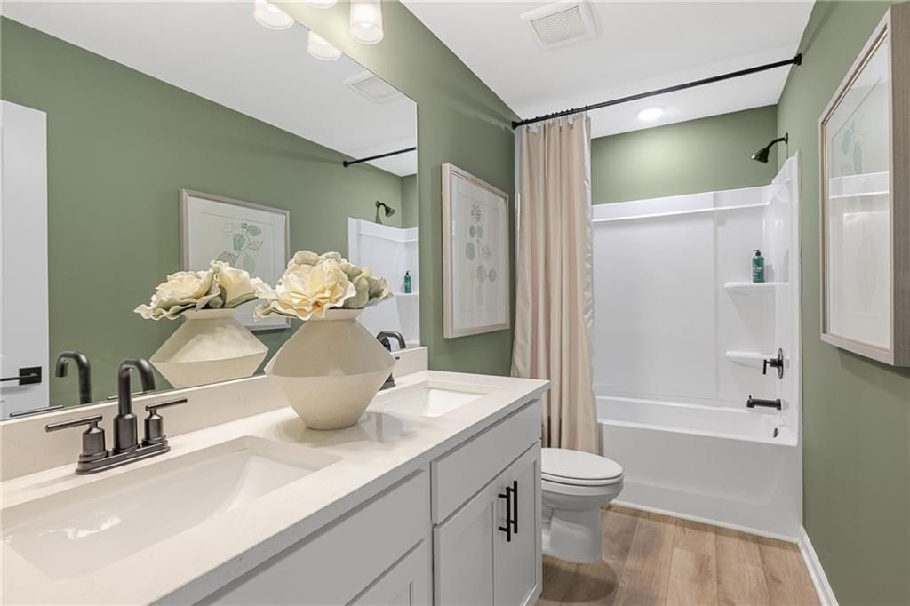Sage green bathroom with double vanity, quartz countertop, tub-shower combo, and wood floors in Davidson Homes The Rabun B, Canton, Georgia