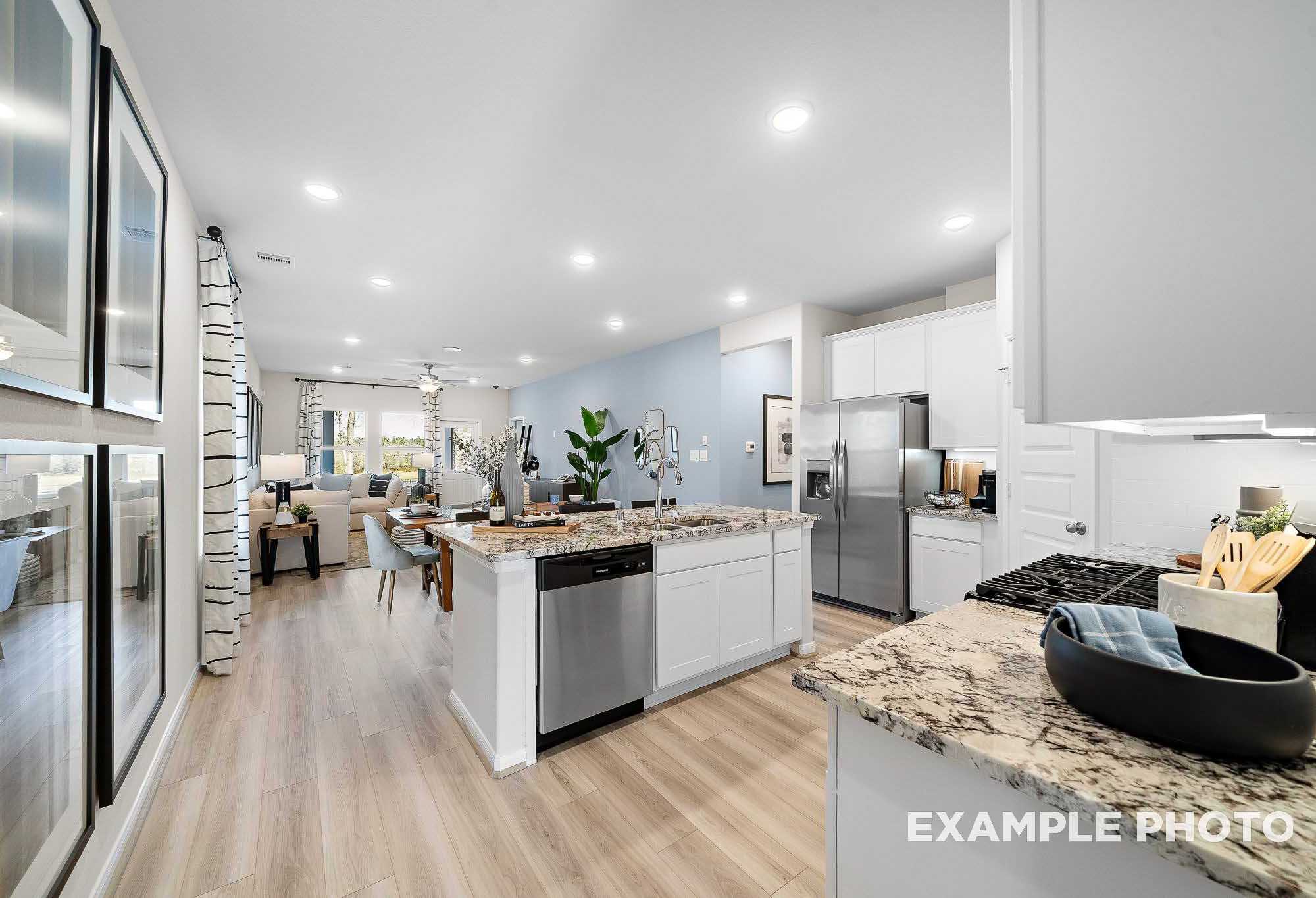 Spacious open-concept kitchen in The San Marcos home with white shaker cabinets, granite island, stainless appliances, and hardwood floors