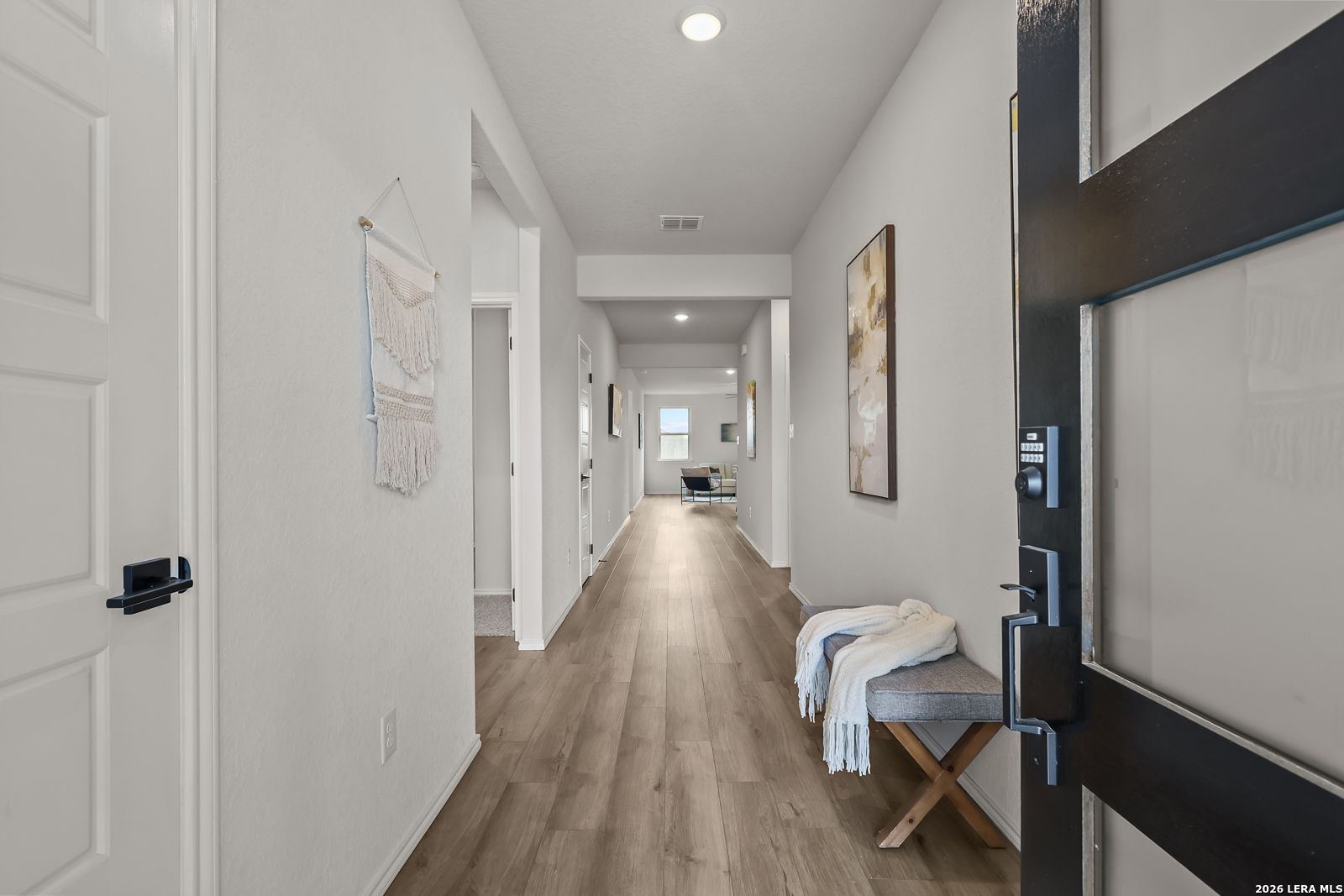 Bright hallway with light oak floors, white walls, wall art, and entry bench in Davidson Homes The Daphne H, Seguin, Texas