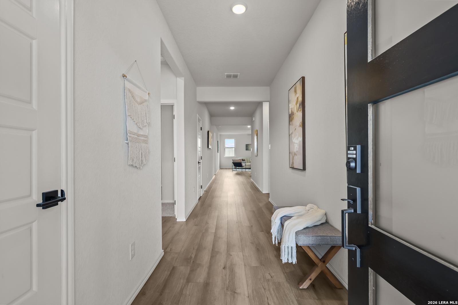 Bright hallway with light oak floors, white walls, wall art, and entry bench in Davidson Homes The Daphne H, Seguin, Texas