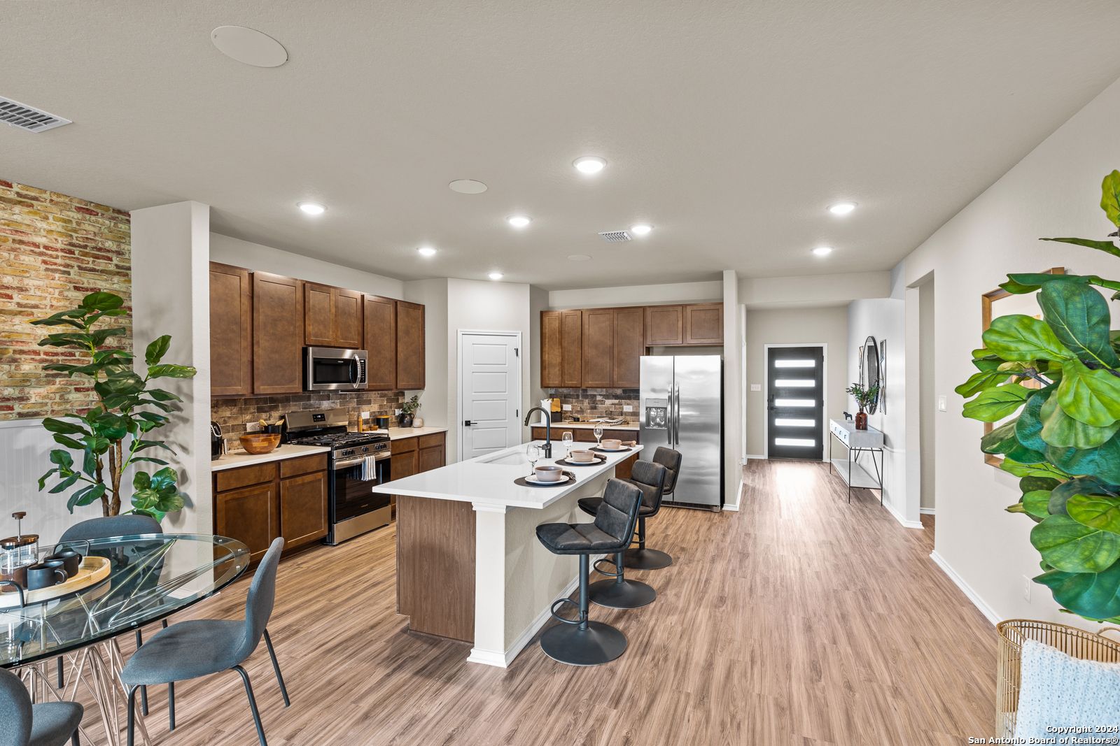 Modern open-concept kitchen with white island, wood cabinets, stainless appliances, and dining nook in Davidson Homes The Douglas F, Bricewood, San Antonio
