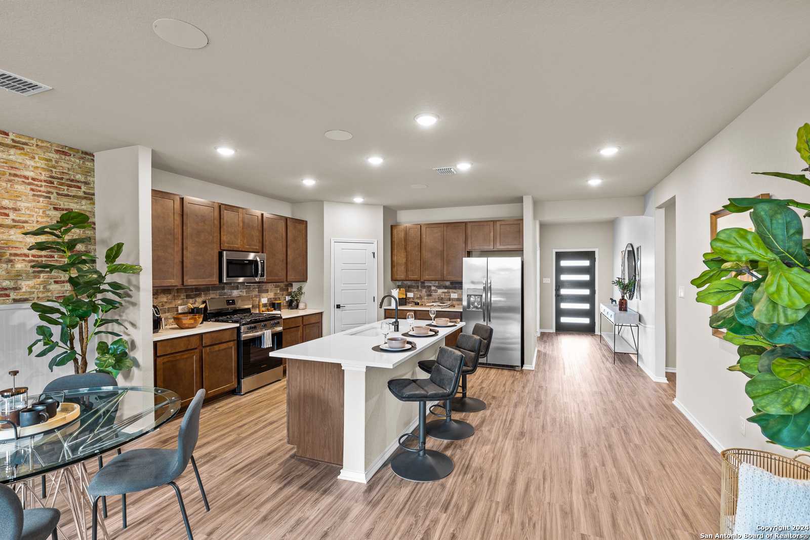 Modern open-concept kitchen with white island, wood cabinets, stainless appliances, and dining nook in Davidson Homes The Douglas F, Bricewood, San Antonio