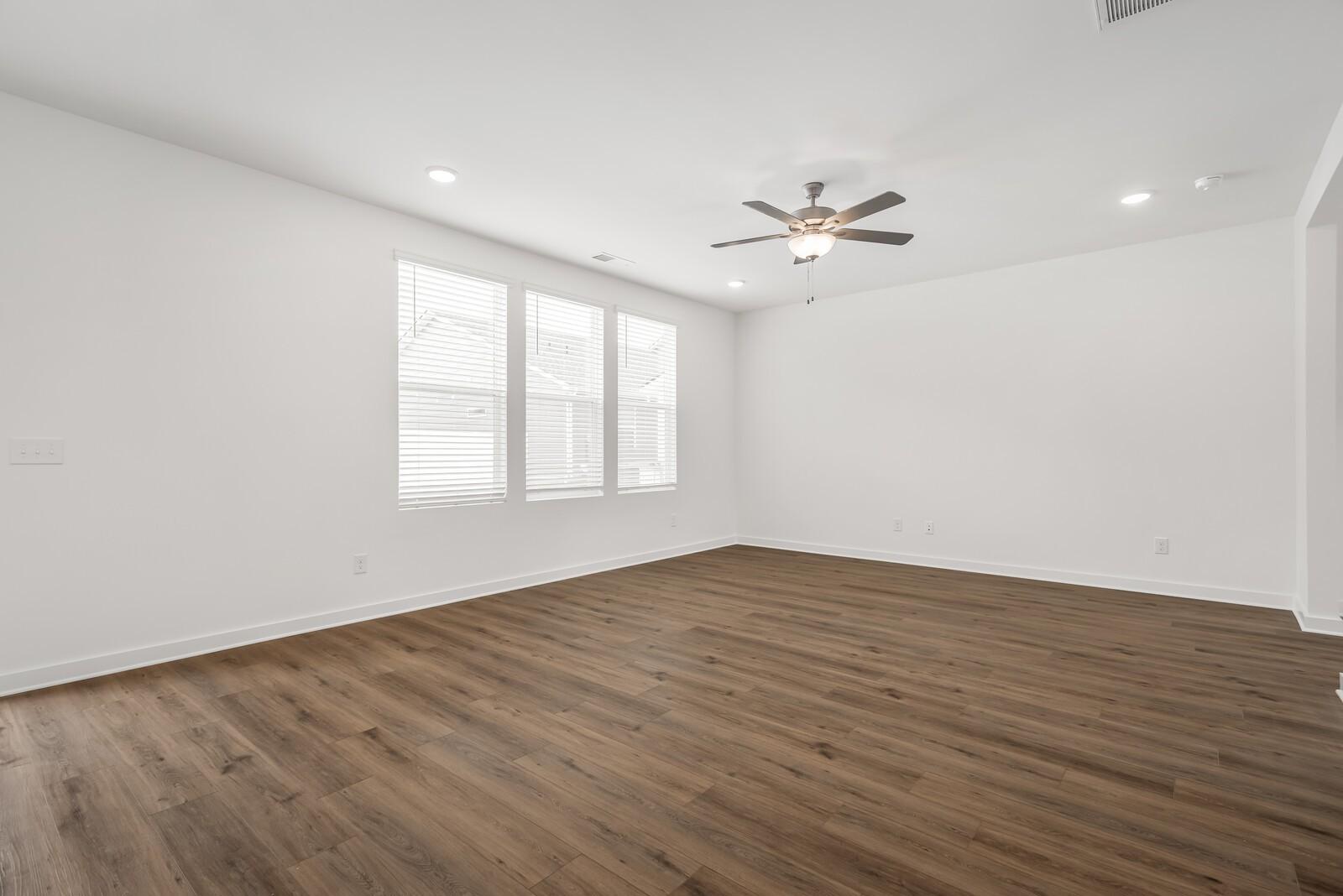 Bright empty living room with large windows, ceiling fan, recessed lights, and hardwood floors in Davidson Homes The Gordon C, White House, TN