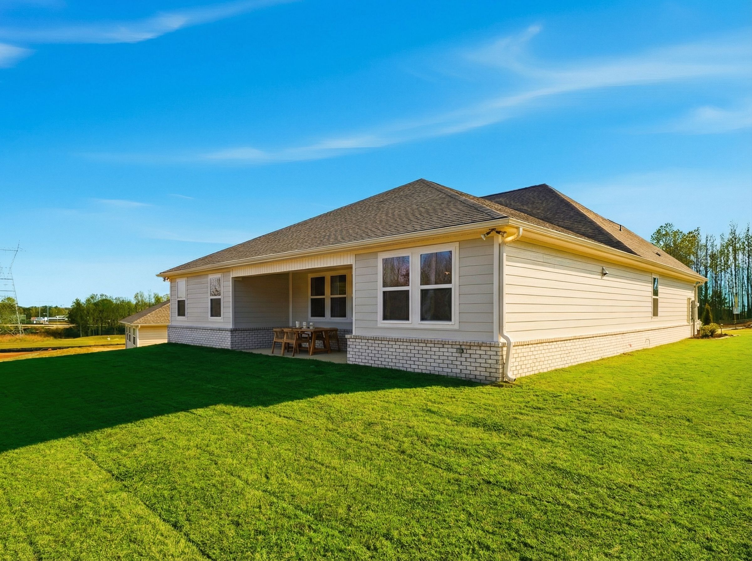 Side elevation of The Hibiscus F single-story home with beige siding, brick accents, covered porch, and lush green lawn in Cullman, AL