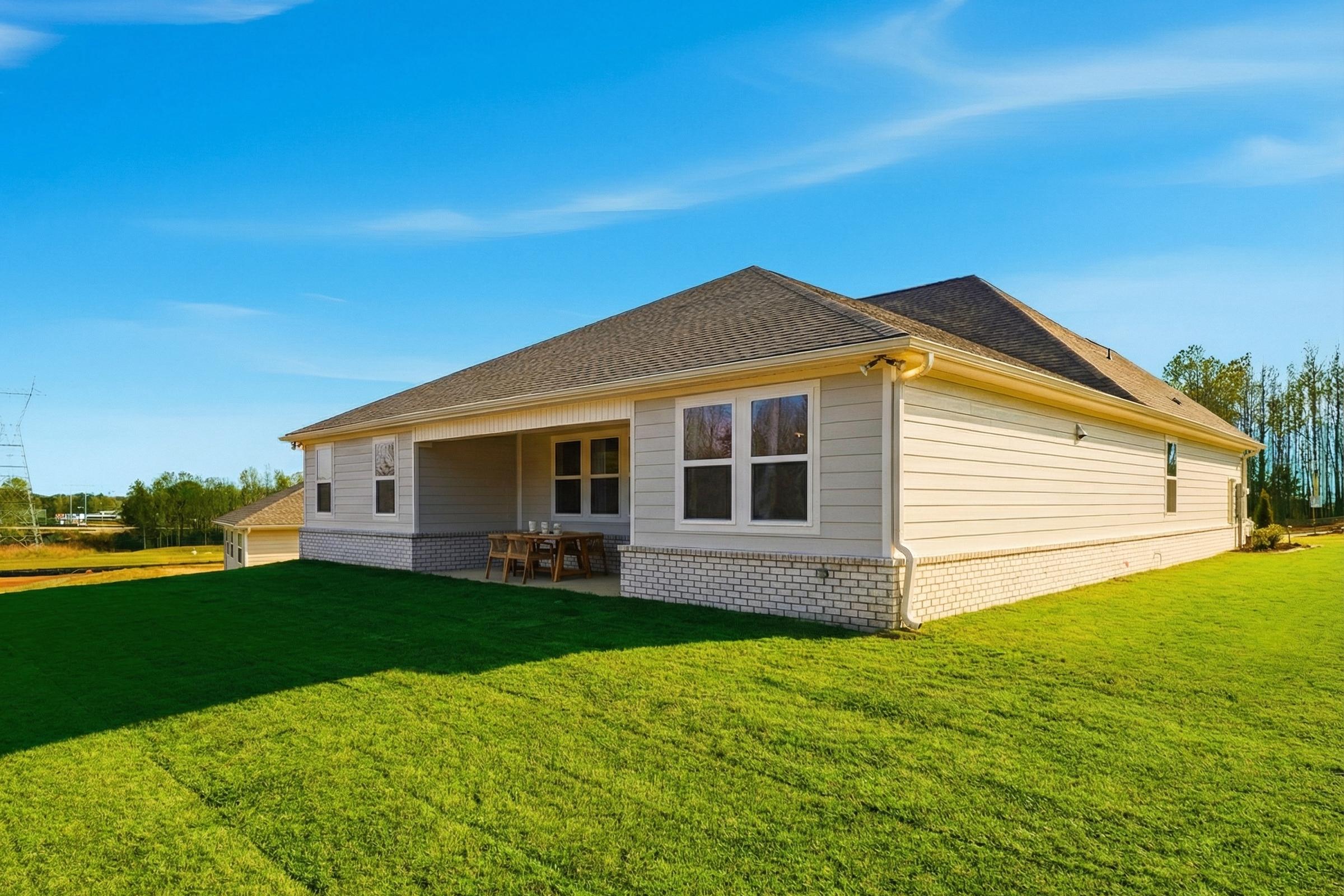 Side elevation of The Hibiscus F single-story home with beige siding, brick accents, covered porch, and lush green lawn in Cullman, AL