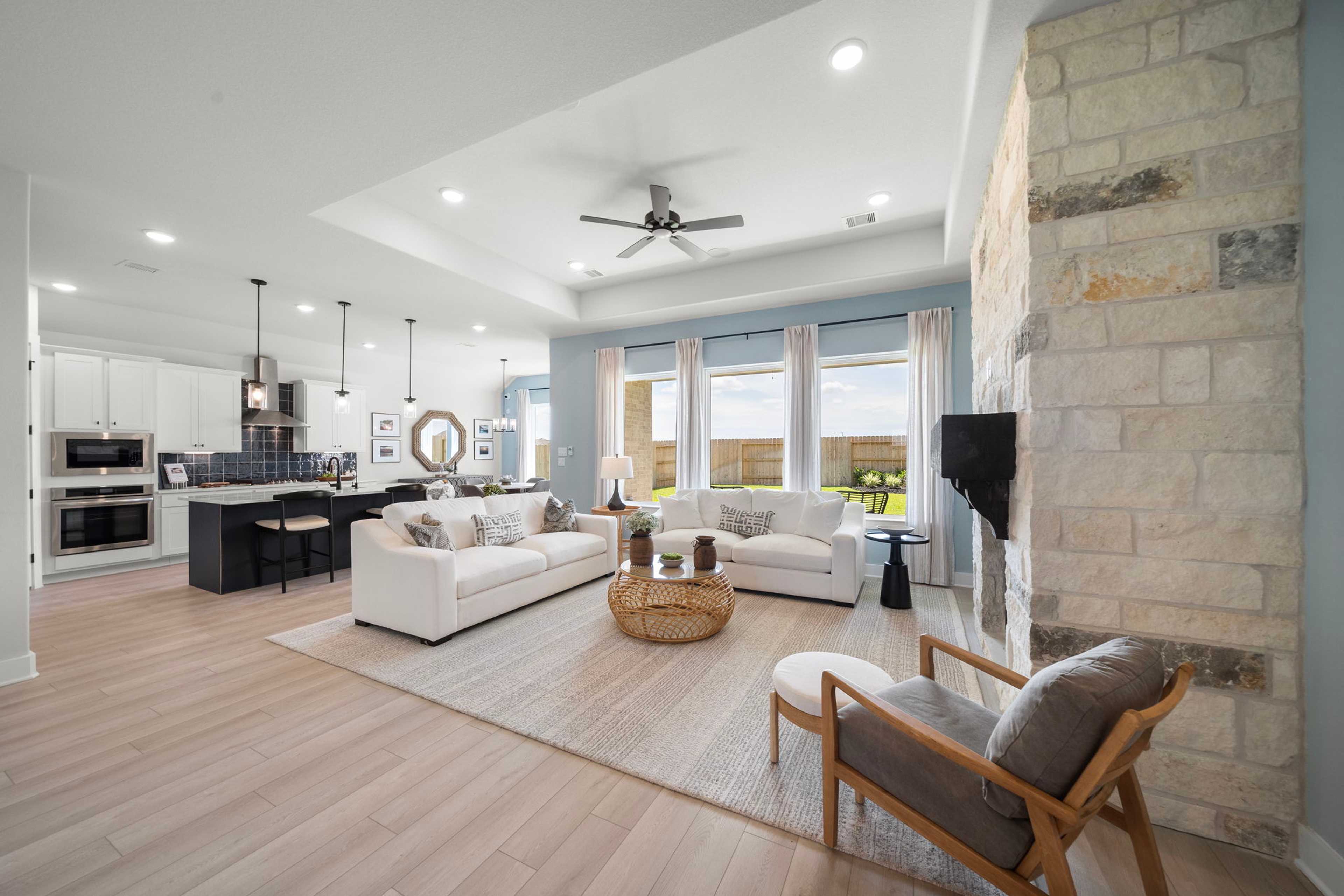 Open-concept living room and kitchen in Lago Mar by Davidson Homes, Texas City TX featuring stone fireplace, hardwood floors, large windows