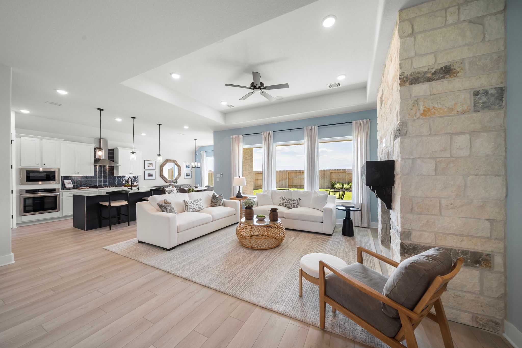 Open-concept living room and kitchen in Lago Mar by Davidson Homes, Texas City TX featuring stone fireplace, hardwood floors, large windows