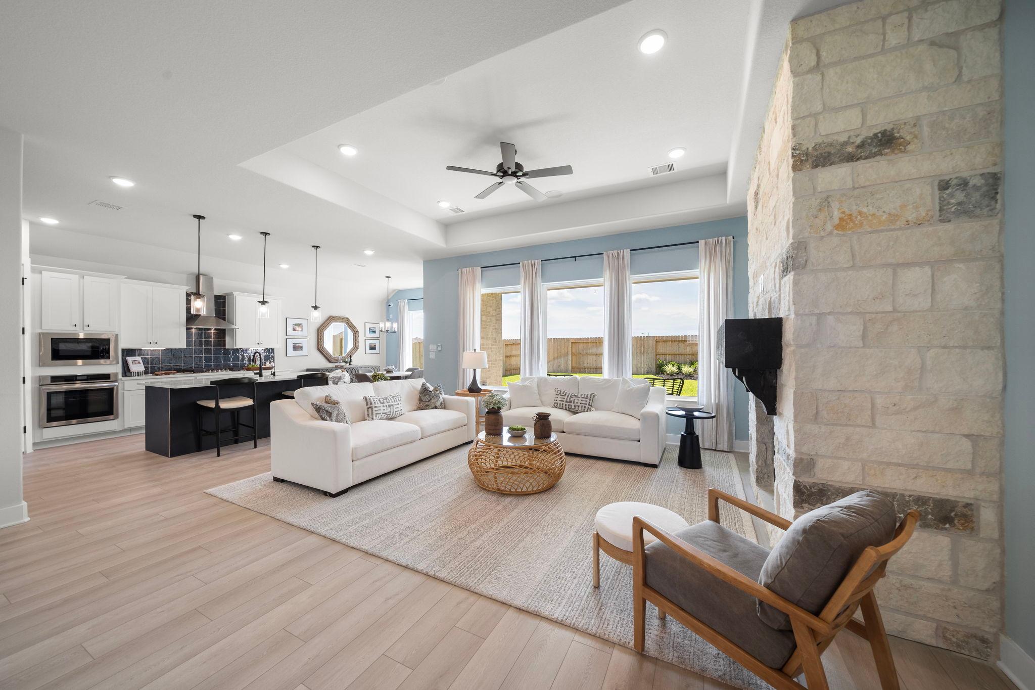 Open-concept living room and kitchen in Lago Mar by Davidson Homes, Texas City TX featuring stone fireplace, hardwood floors, large windows