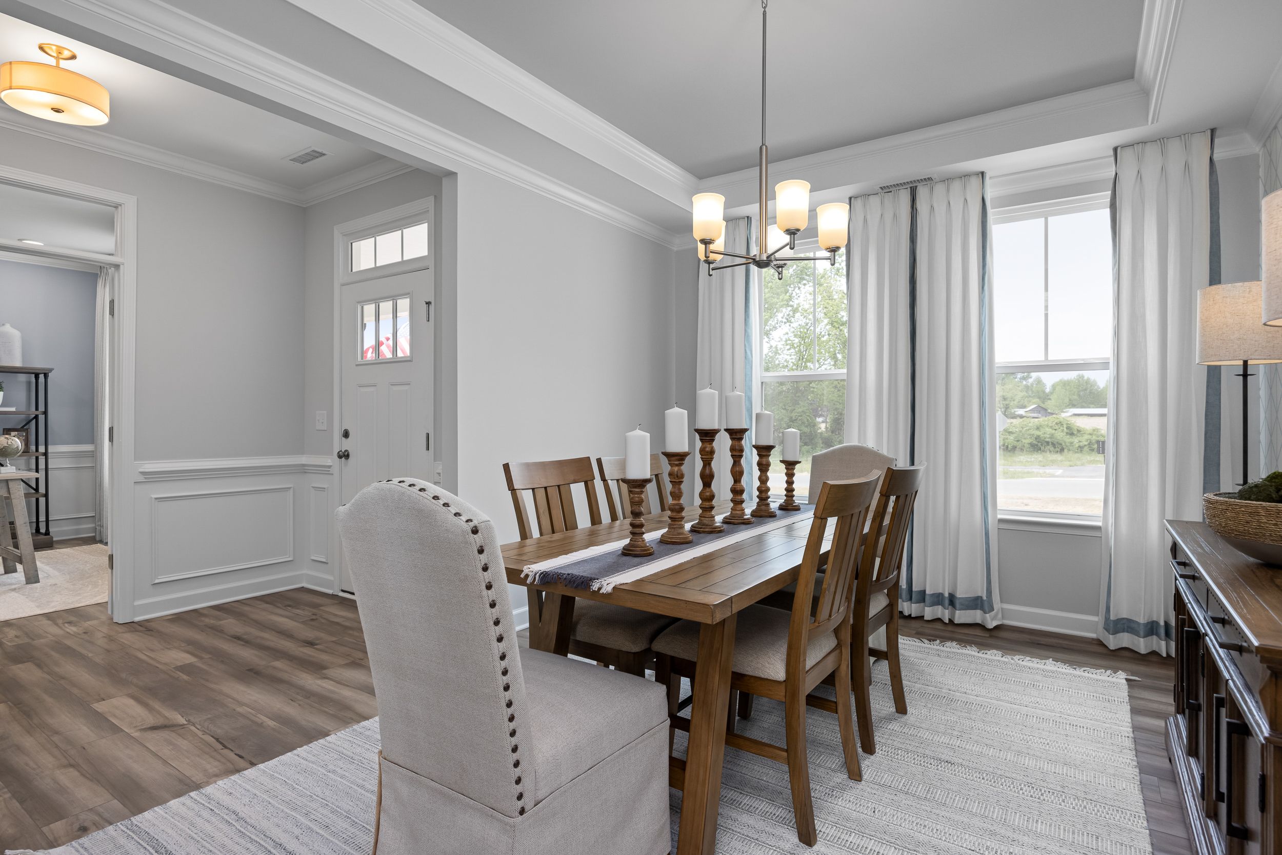 Spacious dining room in The Magnolia B with wooden table, tufted chairs, chandelier, and large curtained windows