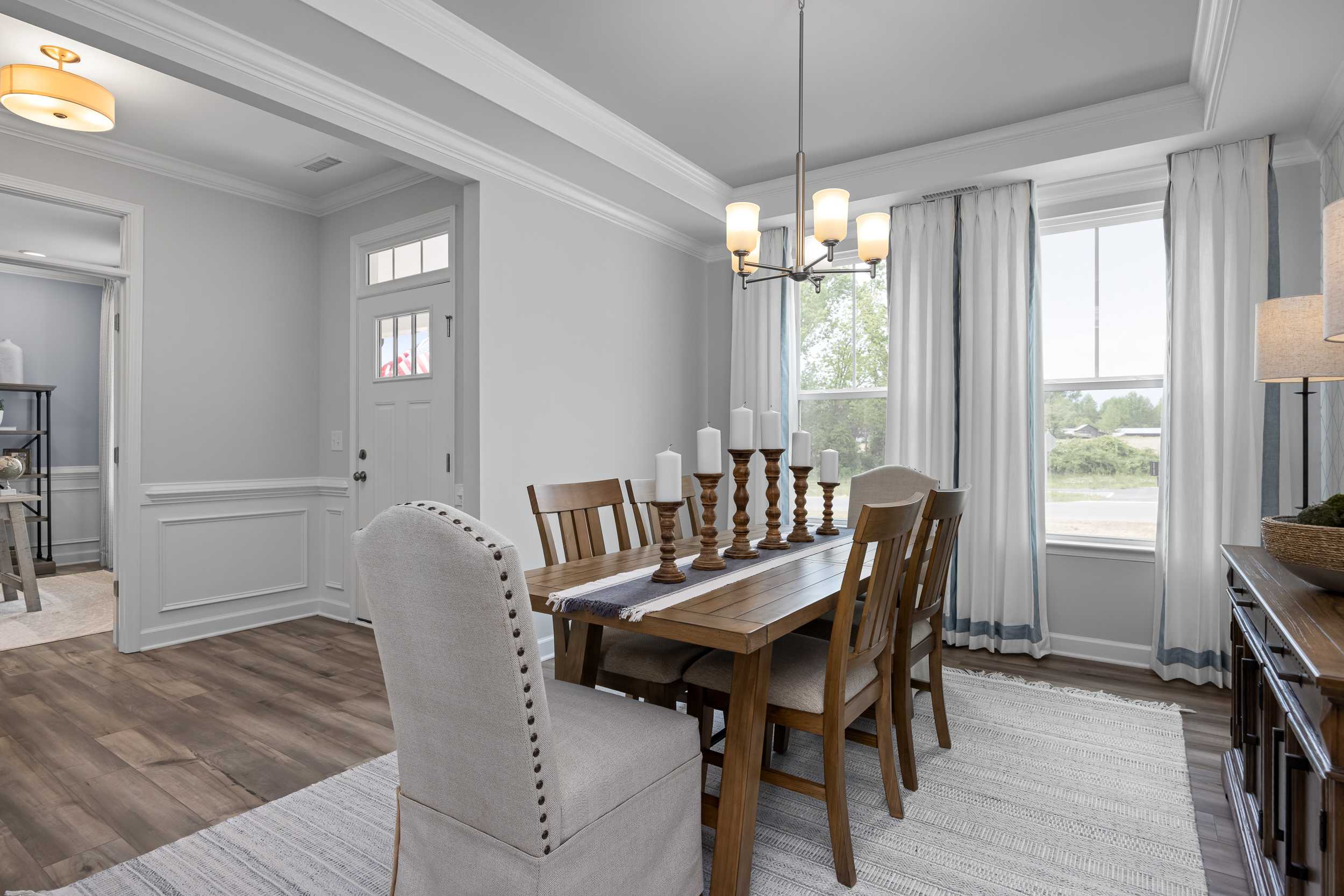 Spacious dining room in The Magnolia A with wooden table, tufted chairs, chandelier, large windows, and open layout in Davidson Homes design