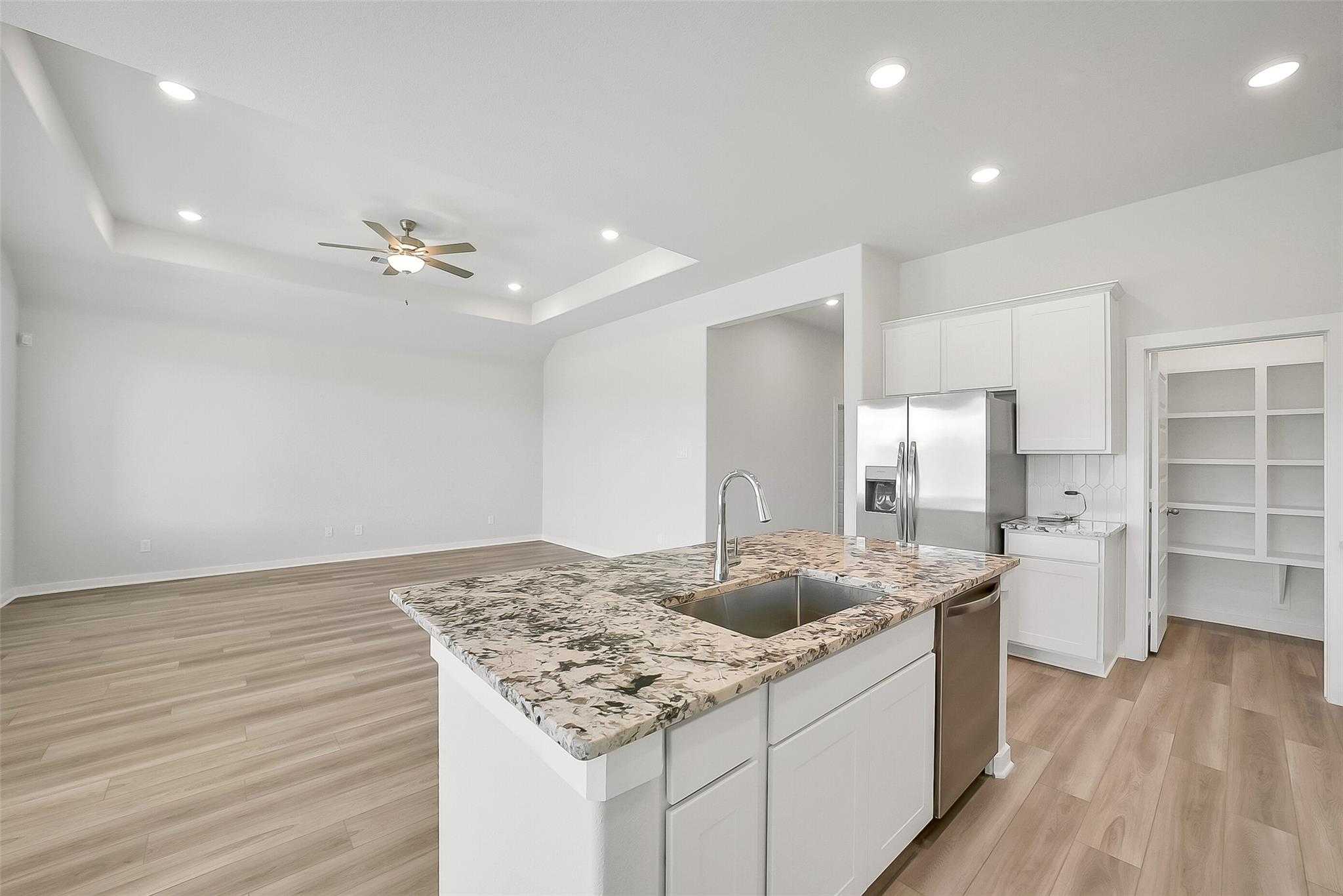 Modern open-concept kitchen with white cabinets, granite island, stainless steel appliances in Davidson Homes Acadia A, Katy TX