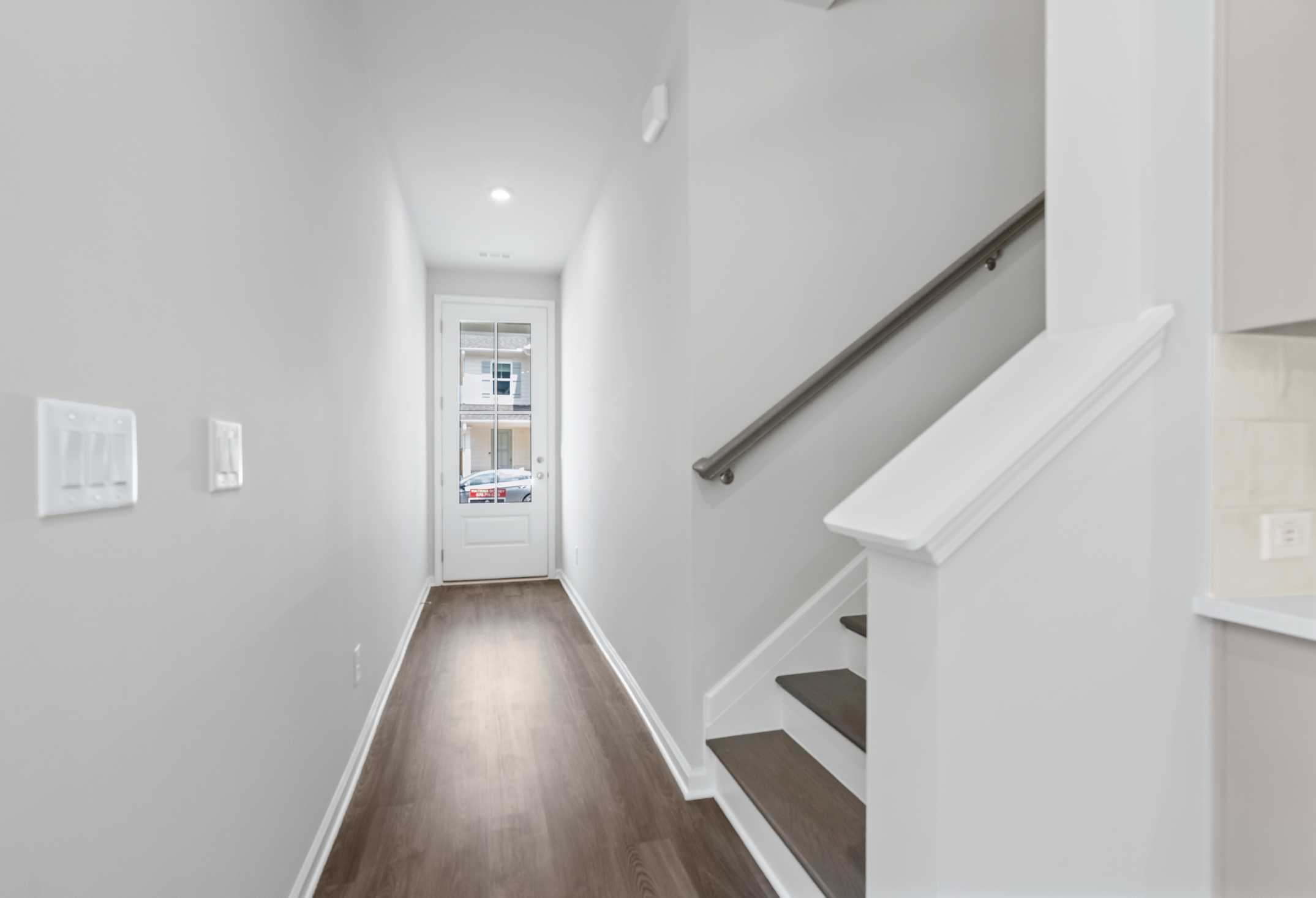 Spacious hallway and staircase in The Cary 2-story home featuring hardwood floors, white railings, and kitchen glimpse