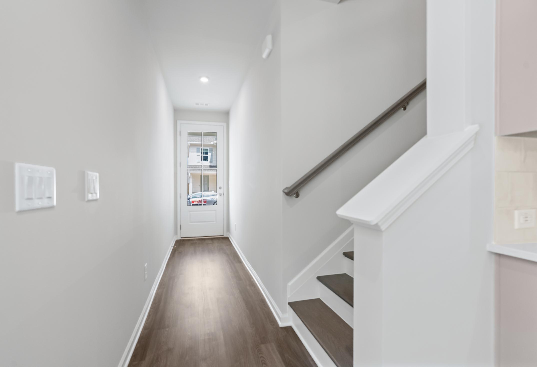 Spacious hallway and staircase in The Cary 2-story home featuring hardwood floors, white railings, and kitchen glimpse