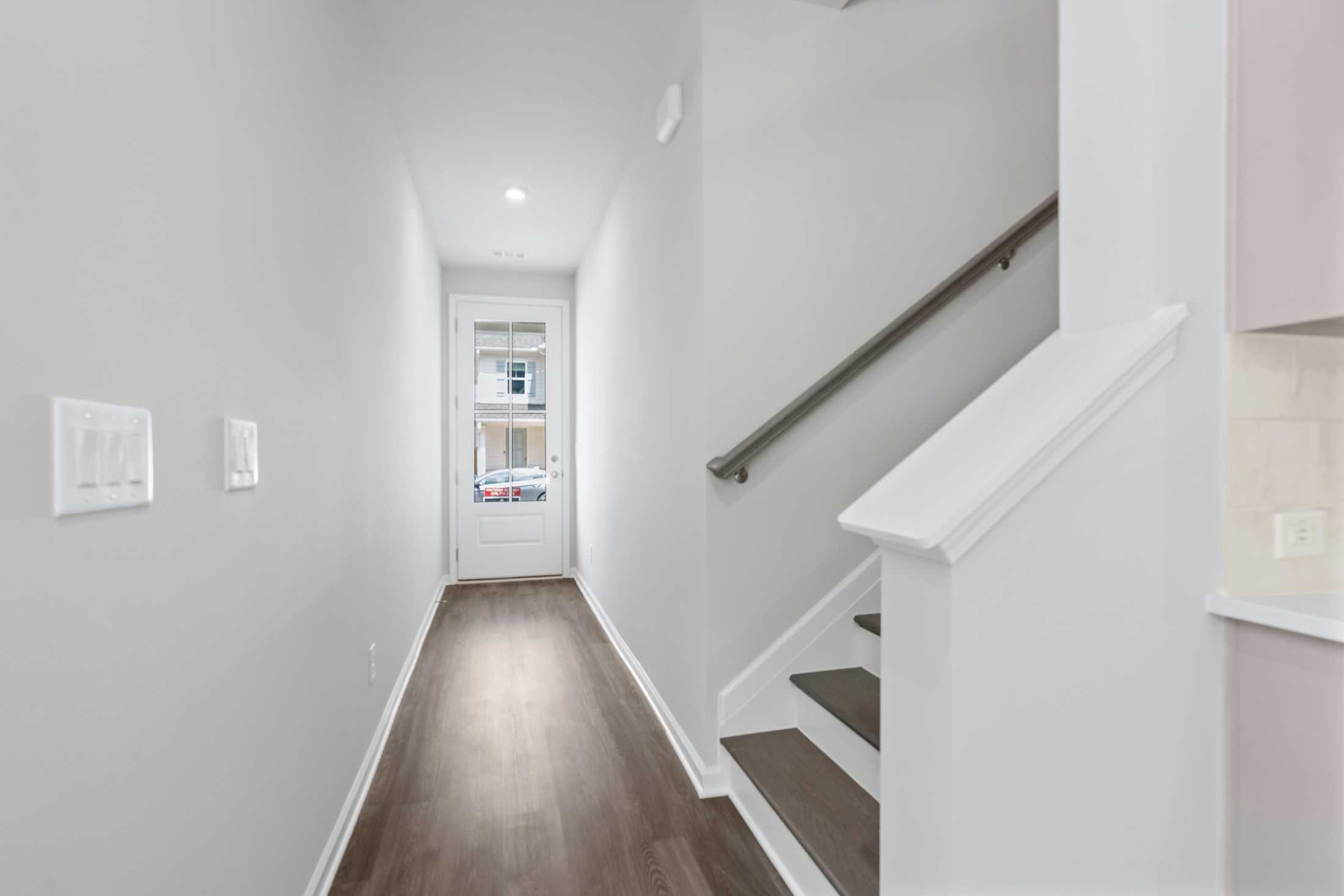 Spacious hallway and staircase in The Cary 2-story home featuring hardwood floors, white railings, and kitchen glimpse