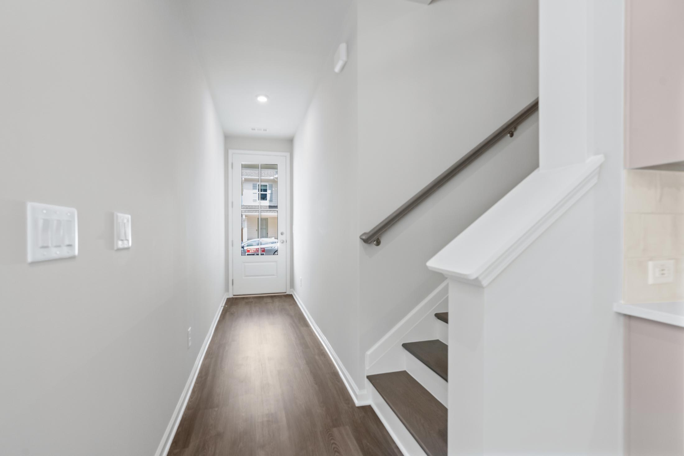 Spacious hallway and staircase in The Cary 2-story home featuring hardwood floors, white railings, and kitchen glimpse