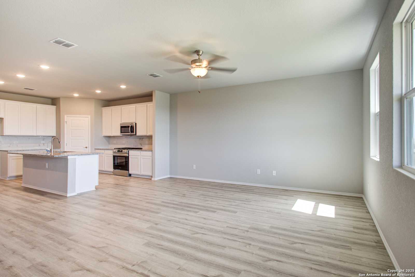 Spacious open kitchen with white cabinets, large island, stainless appliances, and light wood floors in Davidson Homes The Douglas G, San Antonio
