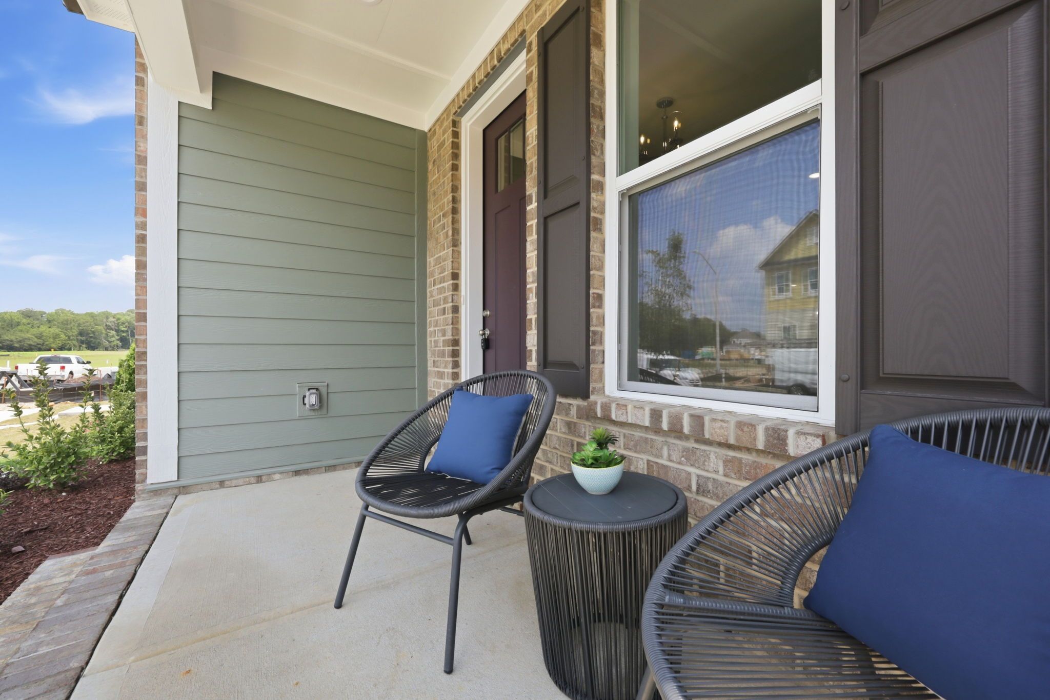 Cozy front porch of The Jordan A in Knightdale, featuring modern outdoor seating, brick accents, and green siding.
