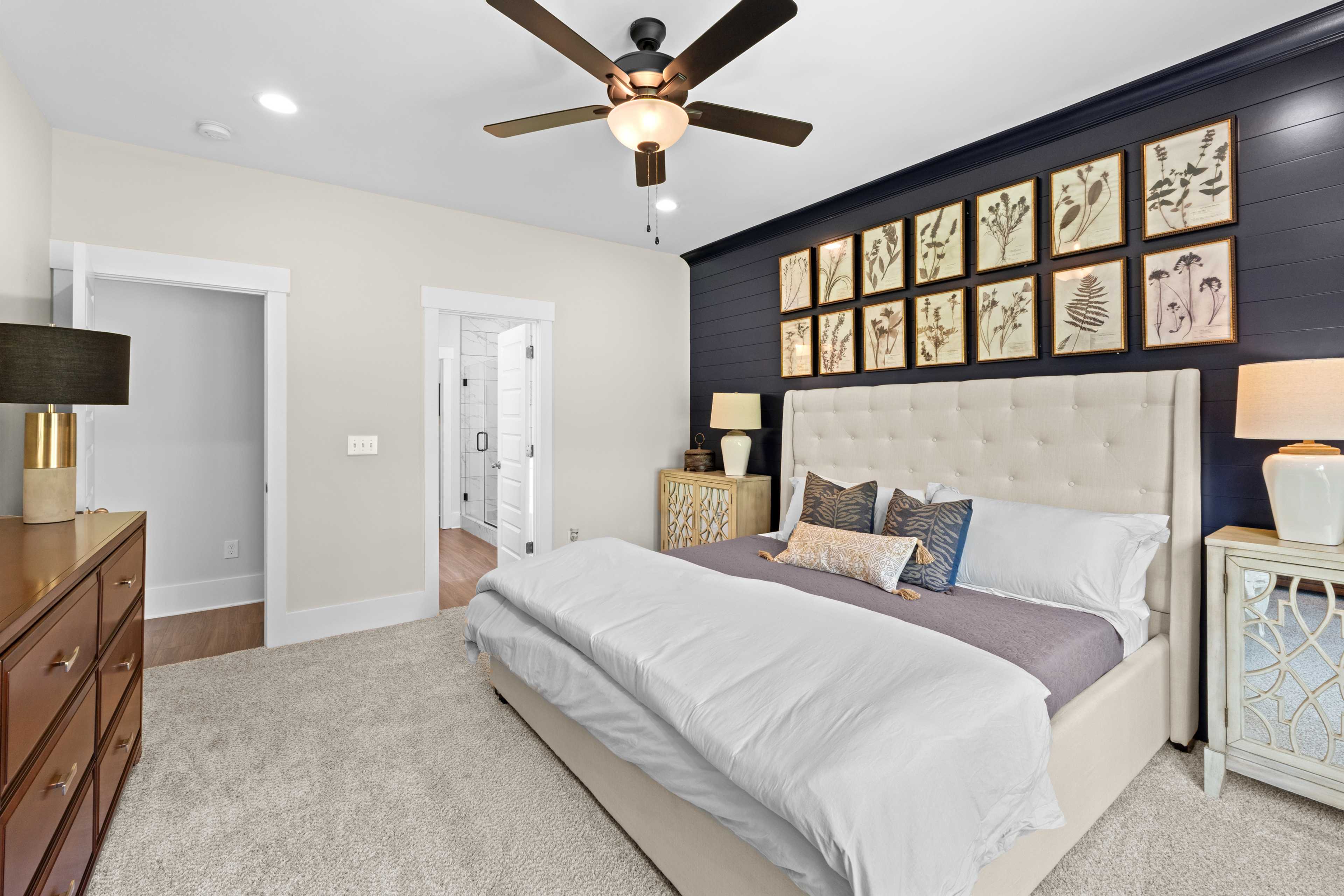 Elegant master bedroom at Ivy Hills in Toney Alabama with navy accent wall, botanical art, king bed, ceiling fan, and carpet flooring