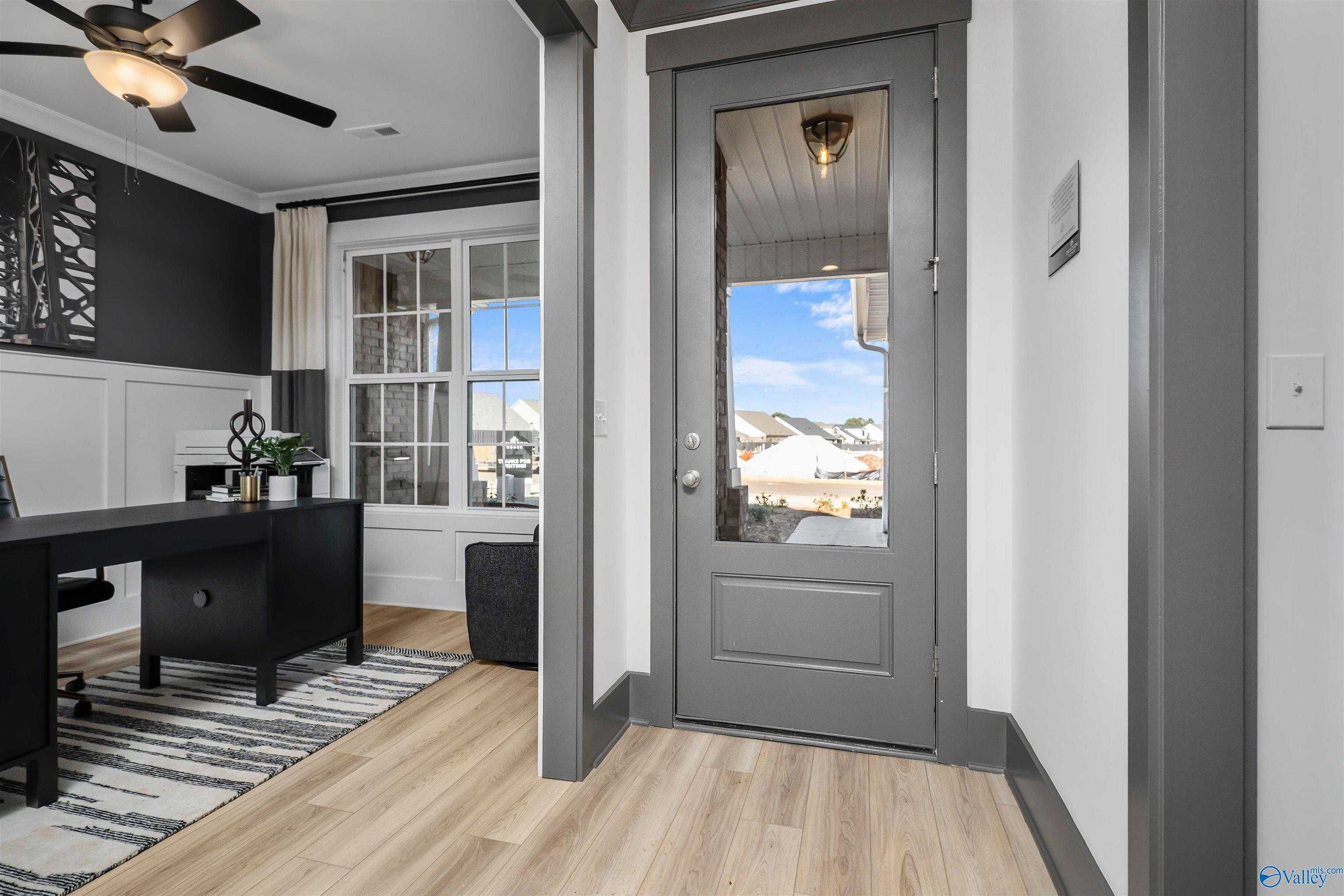 Modern home office with wooden desk, ceiling fan, and glass-paneled door to backyard view in Davidson Homes The Rockford B, Madison AL