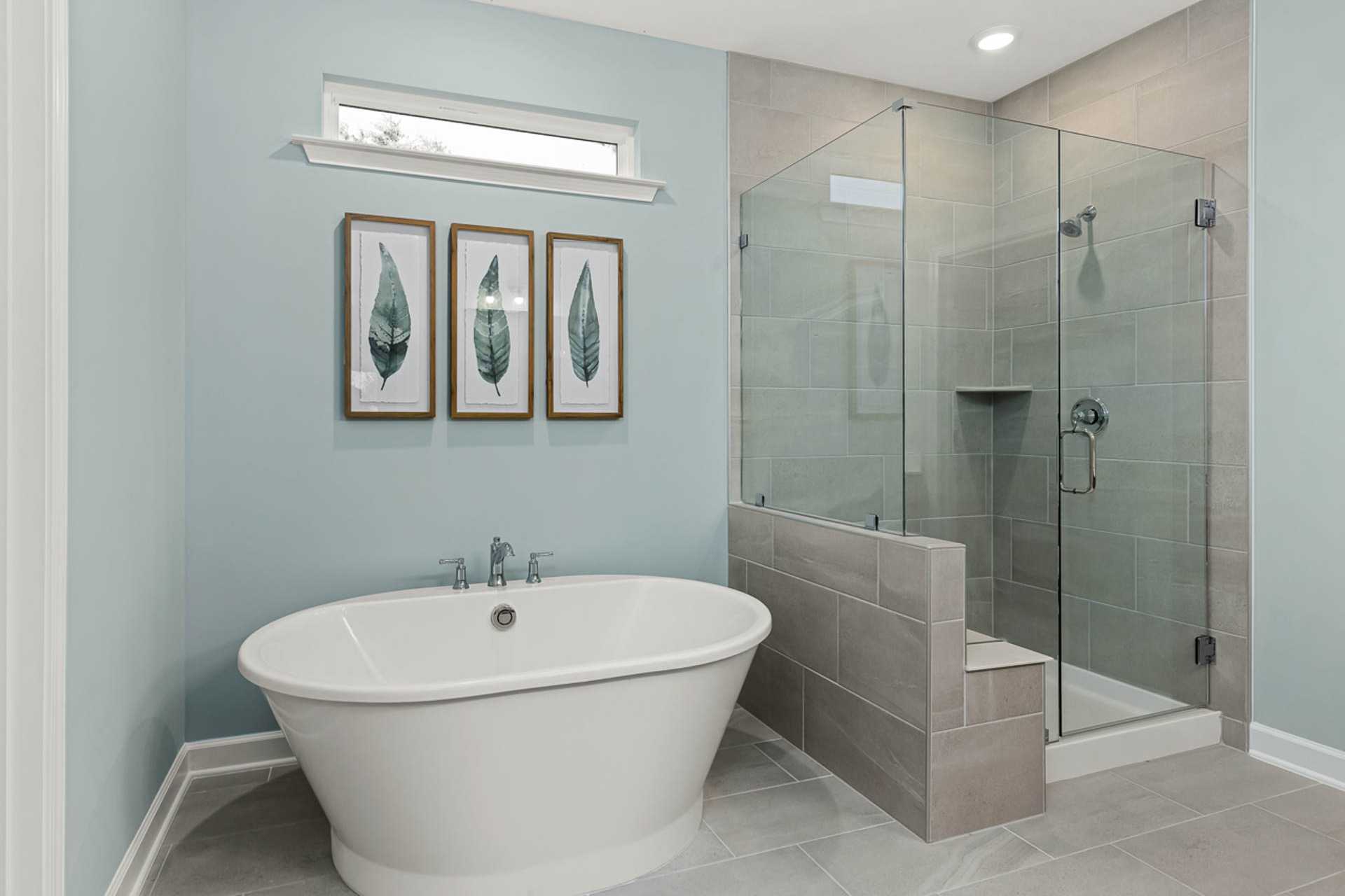 Elegant primary bathroom at Weatherford East in Angier NC with freestanding clawfoot tub, glass shower enclosure, and leaf wall art