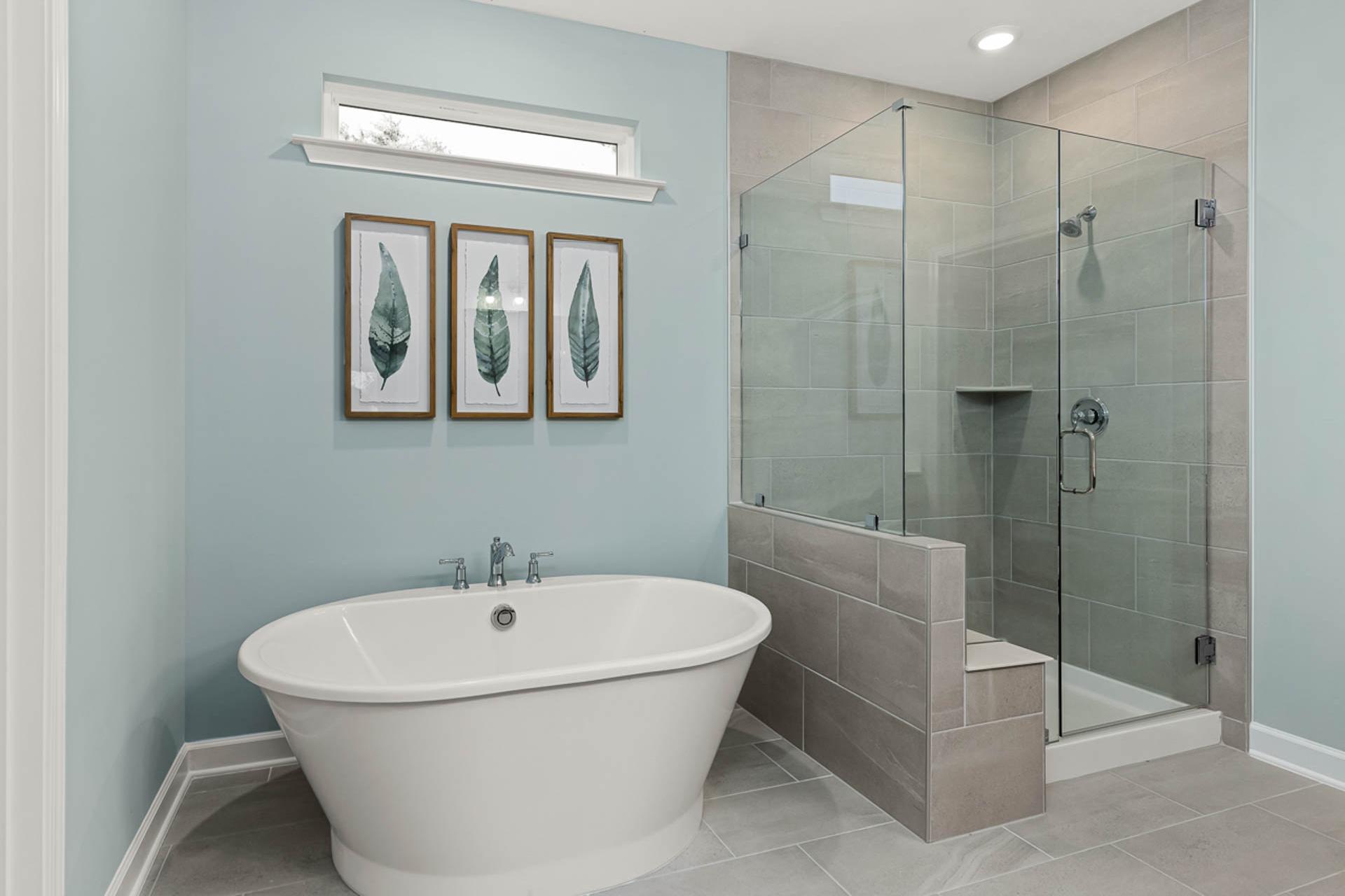 Elegant primary bathroom at Weatherford East in Angier NC with freestanding clawfoot tub, glass shower enclosure, and leaf wall art