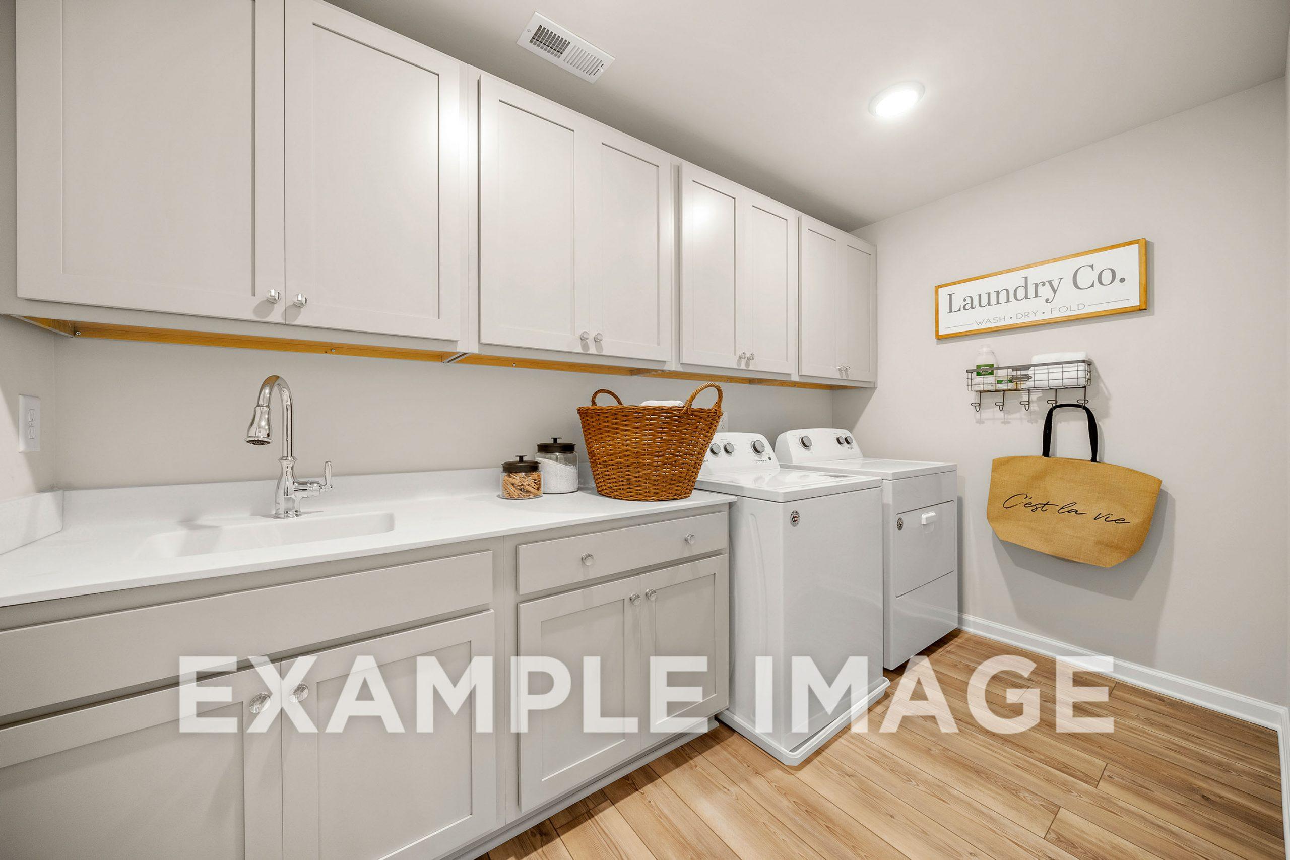 Spacious laundry room in The Hickory B with white shaker cabinets, utility sink, front-load washer dryer, wooden floors