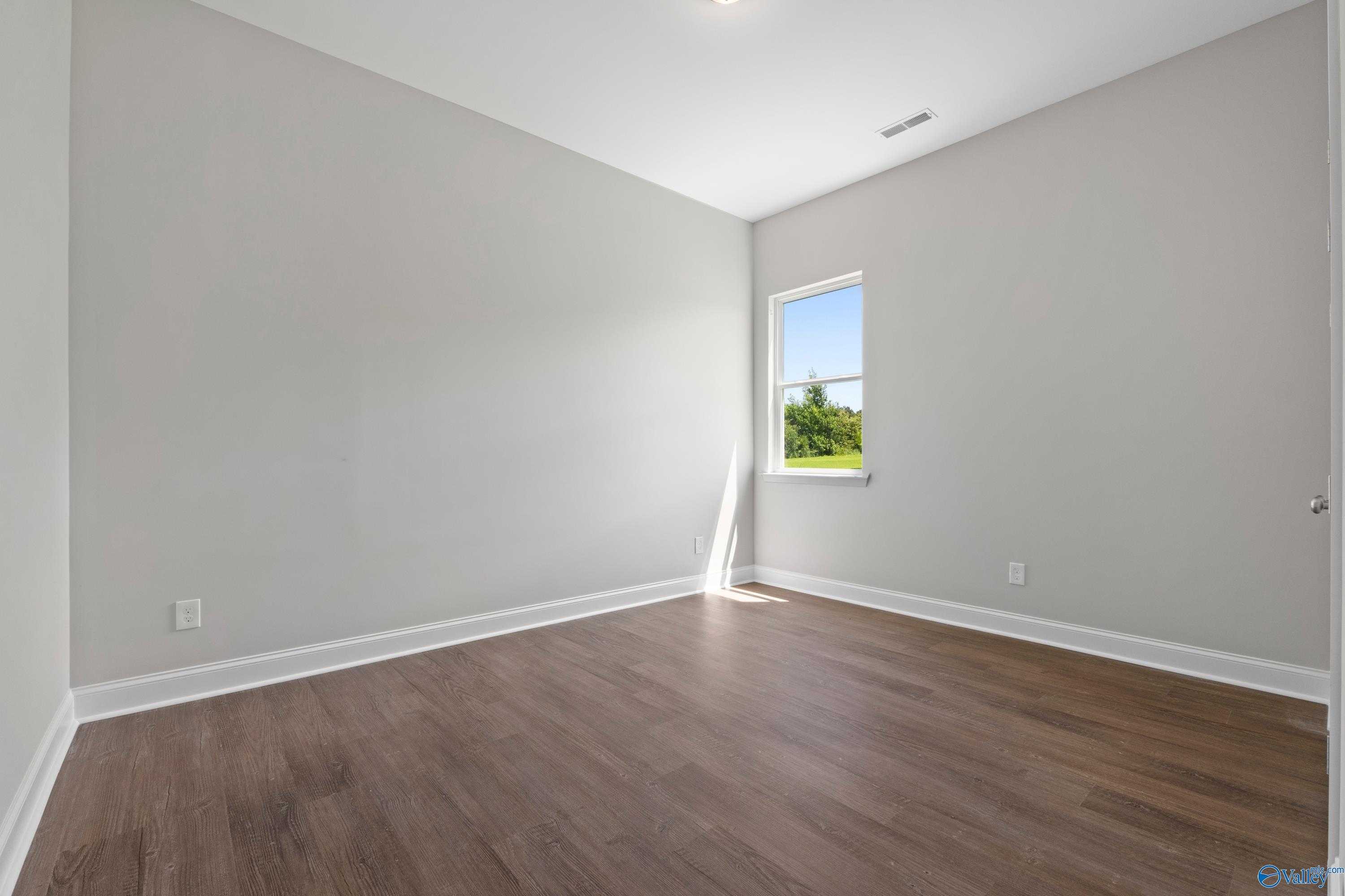 Bright bedroom with light gray walls, hardwood floors, and sunlit window in Davidson Homes The Arcadia, Huntsville, Alabama