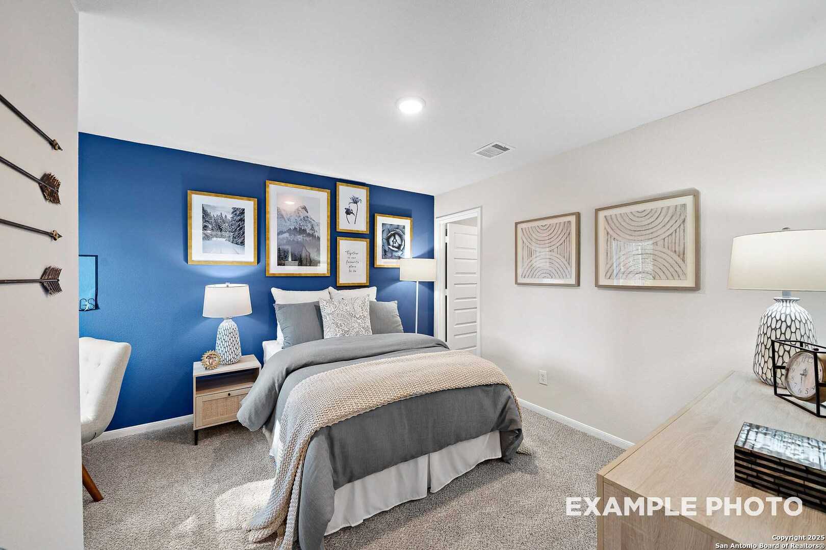 Cozy bedroom with navy accent wall, framed art, arrow decor, gray queen bed, lamps in Davidson Homes The San Marcos D, Agave, San Antonio