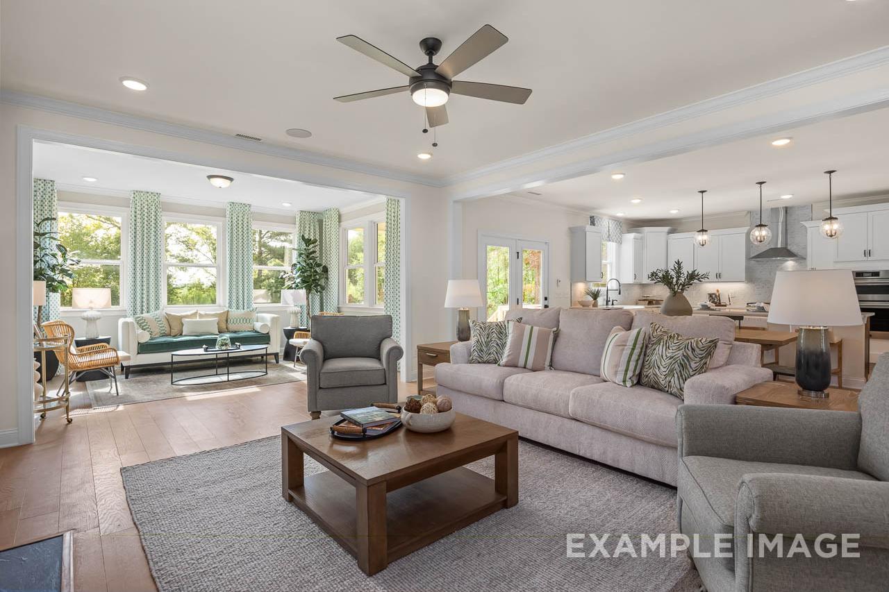 Open-concept living room and kitchen at Wendell Ridge in Wendell, NC by Davidson Homes with hardwood floors, neutral sofas, and large windows