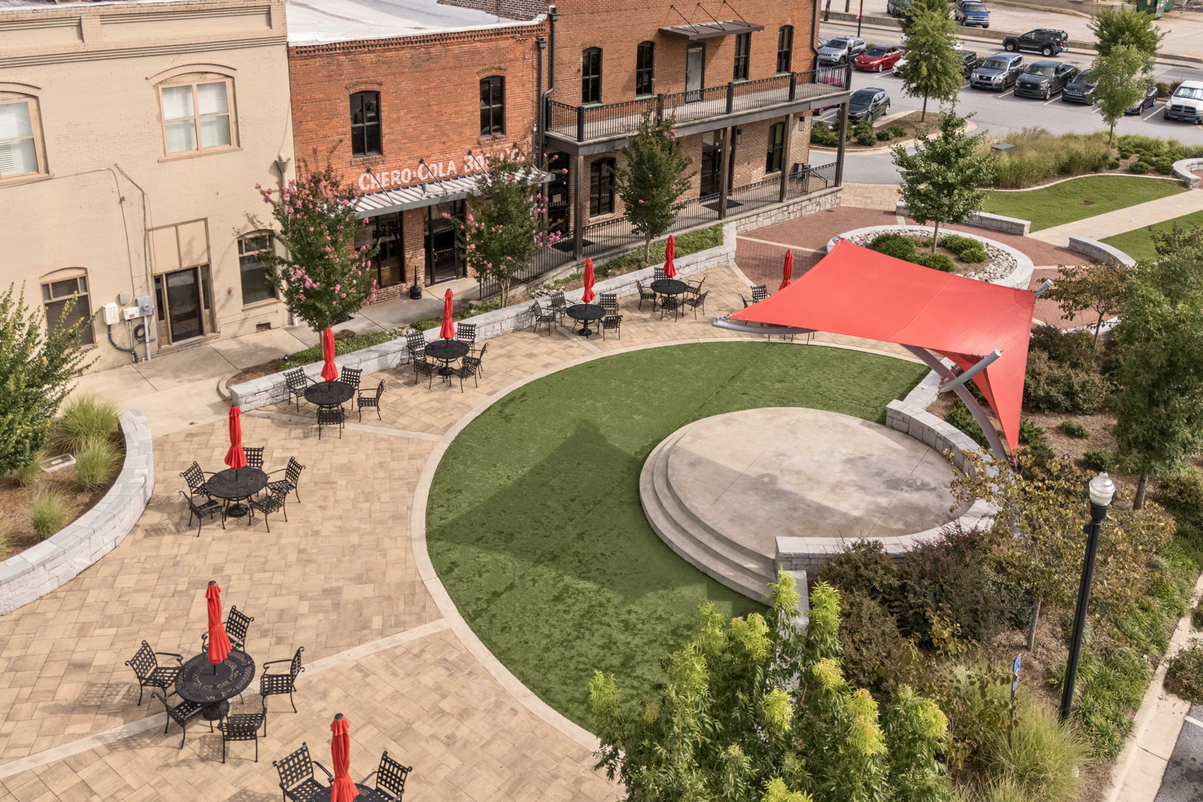 Outdoor plaza at Lake Shore in Winder Georgia with red umbrella tables, central pavilion, brick buildings, and green landscaping